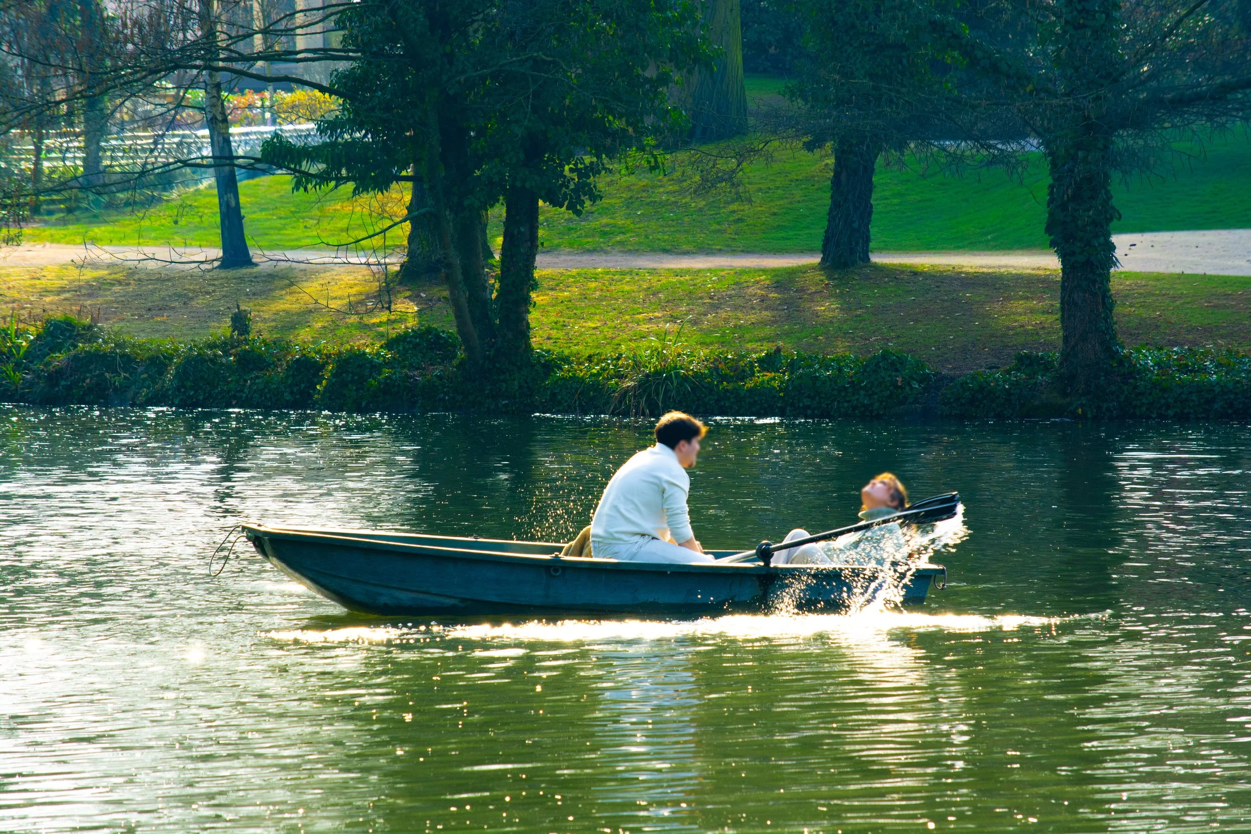 Two people in a small boat on a lake with lush green trees in the background.