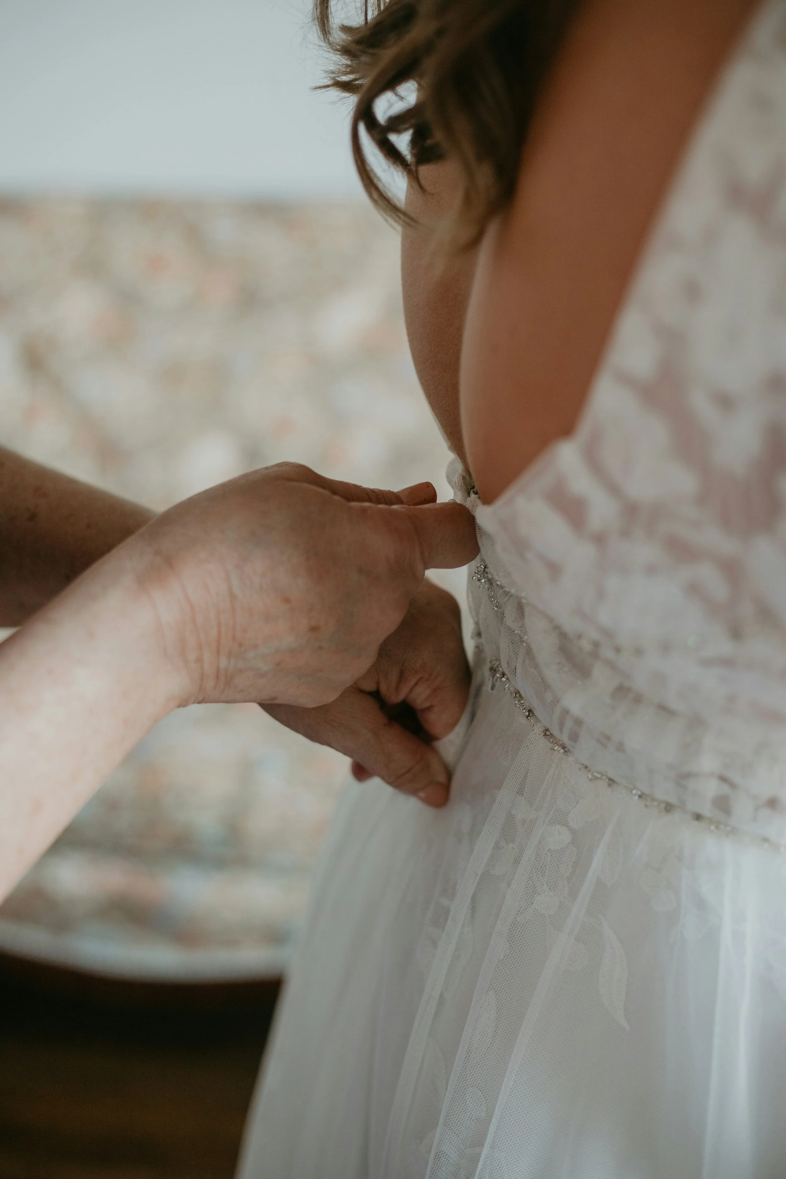 Eine Person wird in einem weißen Hochzeitskleid von einer anderen Person an der Taille gehalten, vermutlich während einer Hochzeit. Der Fokus liegt auf dem Arm und der Hand, die die Taille berühren, mit einem verschwommenen Hintergrund.