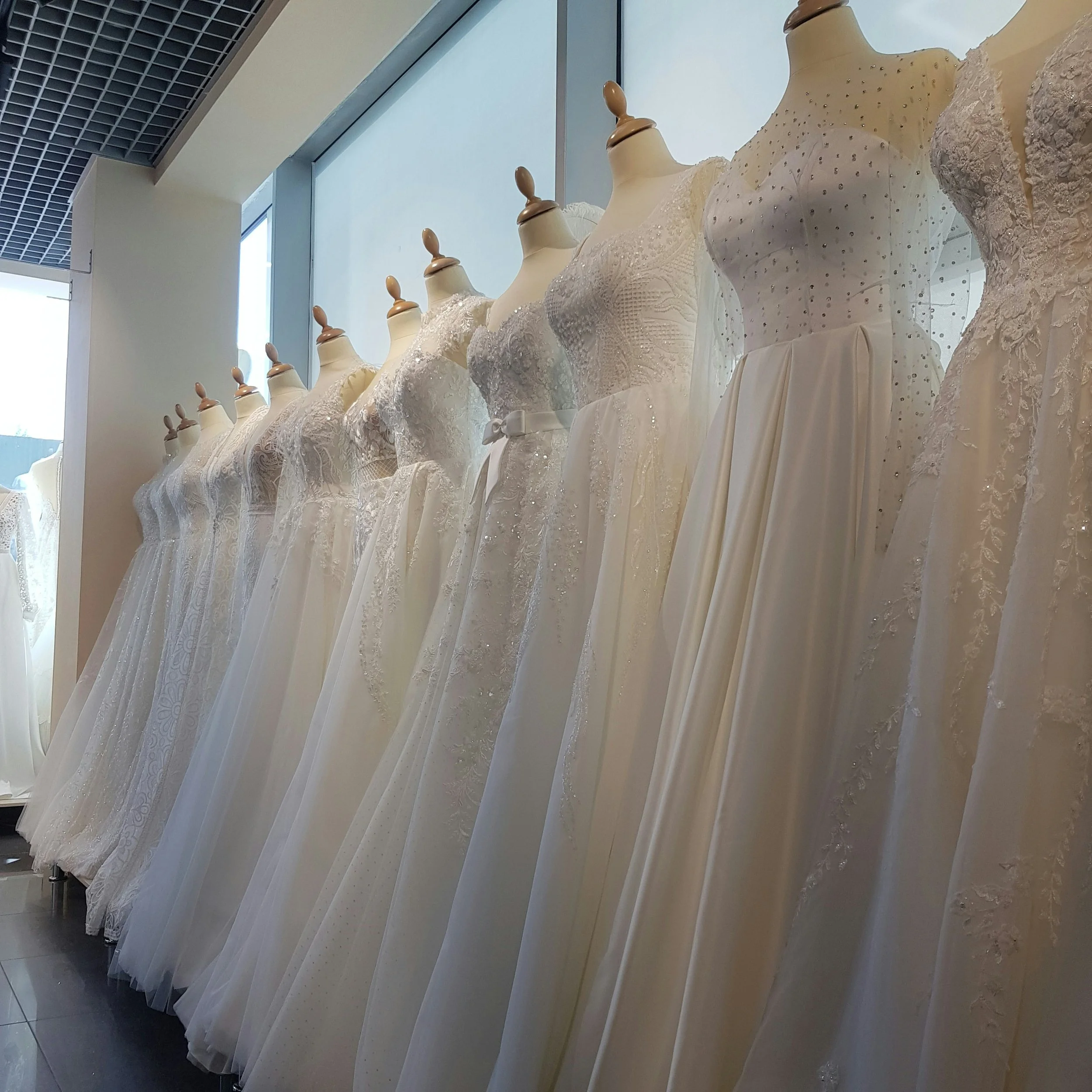 Mehrere elegante weiße Brautkleider auf Kleidervitrinen in einem Ladenfenster ausgestellt.