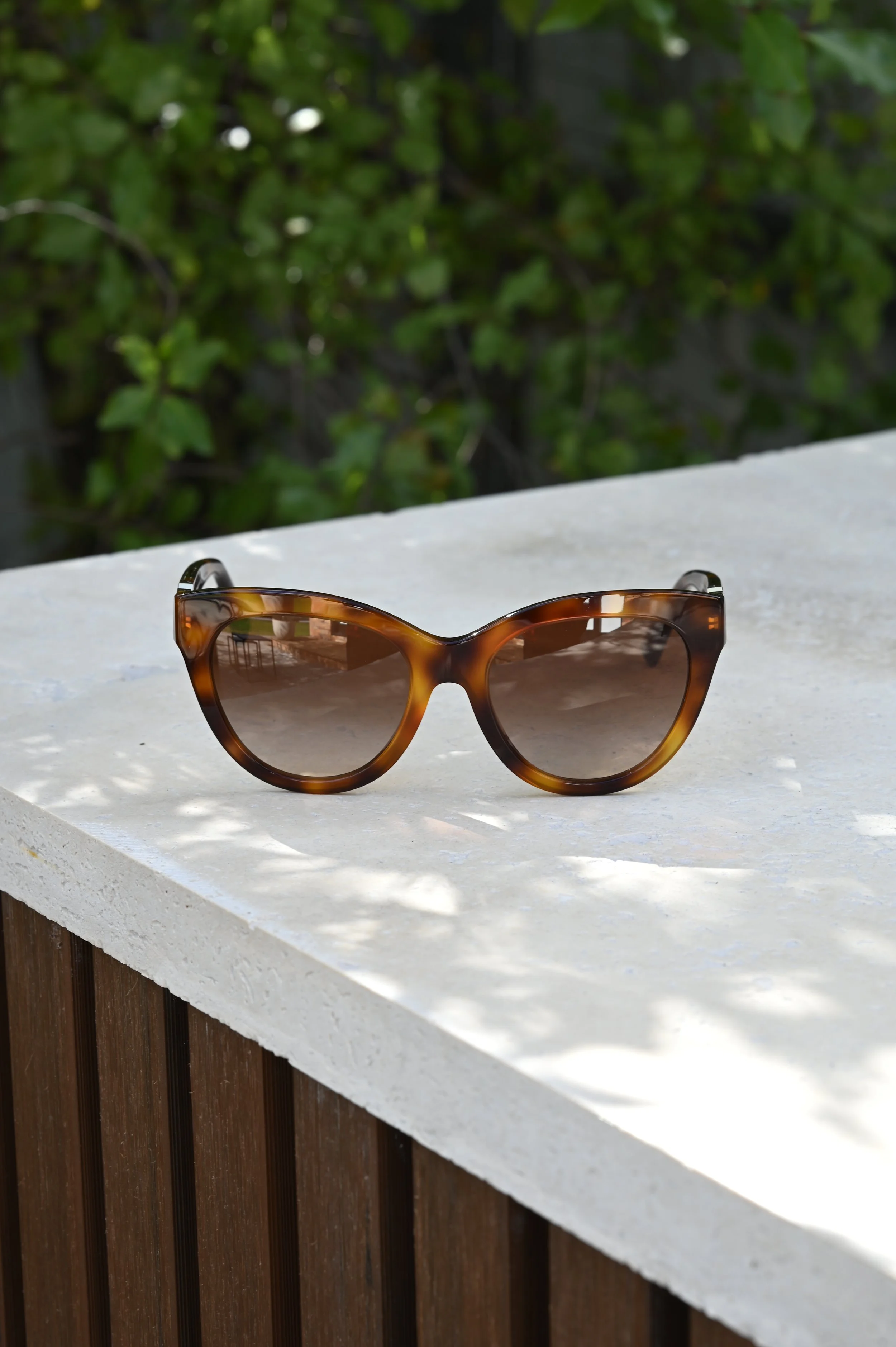 Tortoise shell Valentino sunglasses with brown lenses resting on a white surface, with greenery in the background.