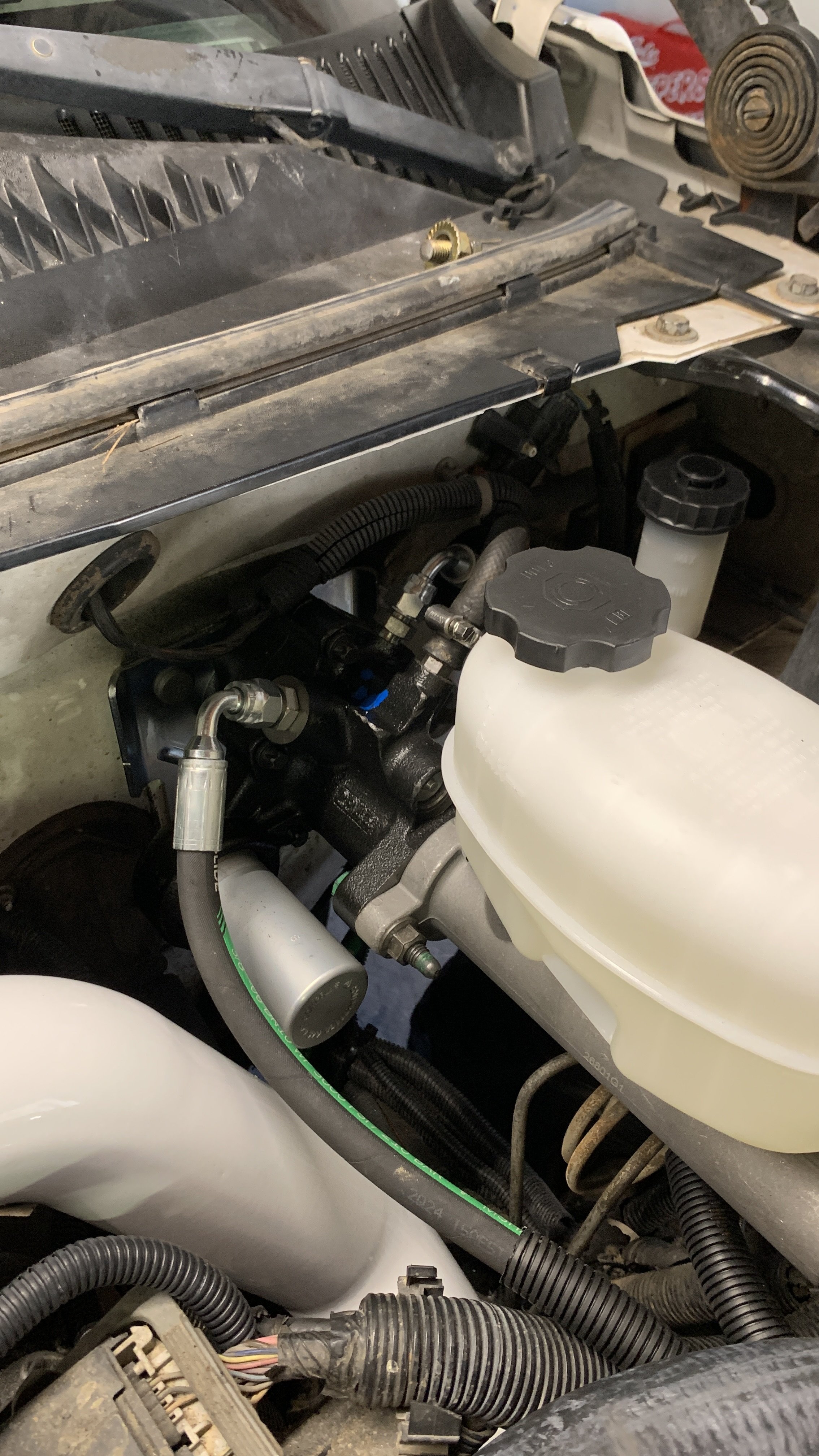 Close-up of a vehicle engine compartment showing a brake fluid reservoir, various hoses, and engine components.