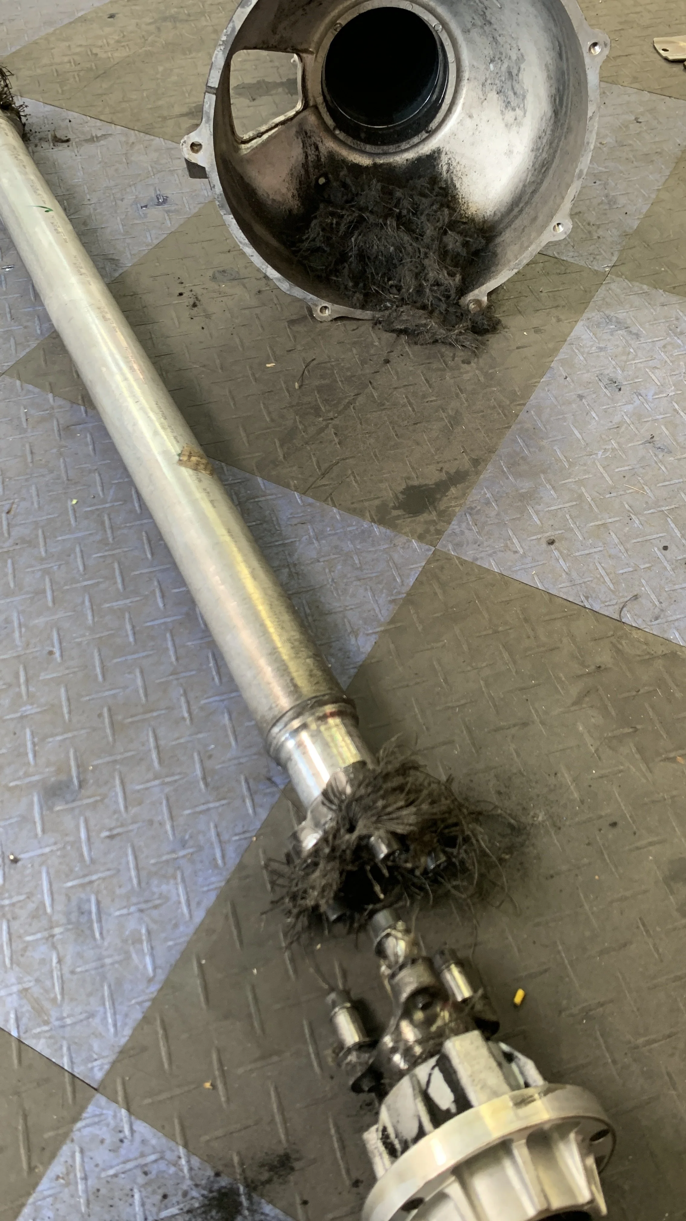 A disassembled driveshaft with a damaged universal joint, lying on a checkered metal garage floor.