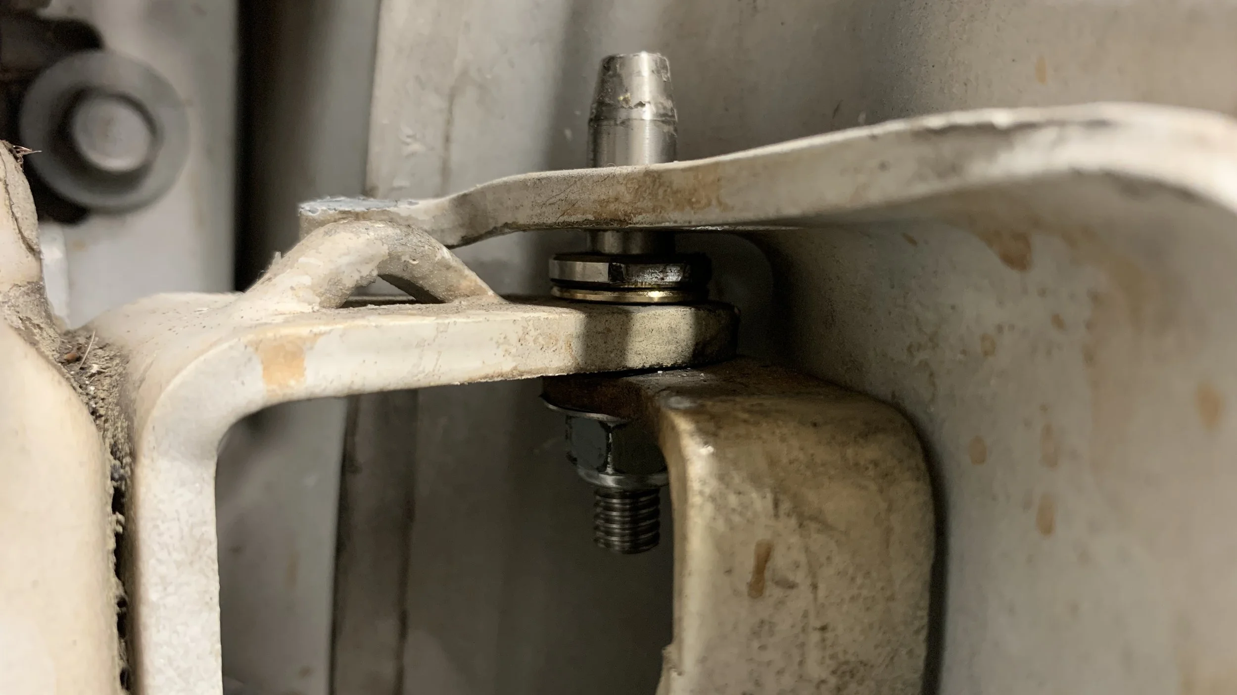 Close-up of a mechanical joint with a bolt and bearing, showing rust and dirt on a metal structure.