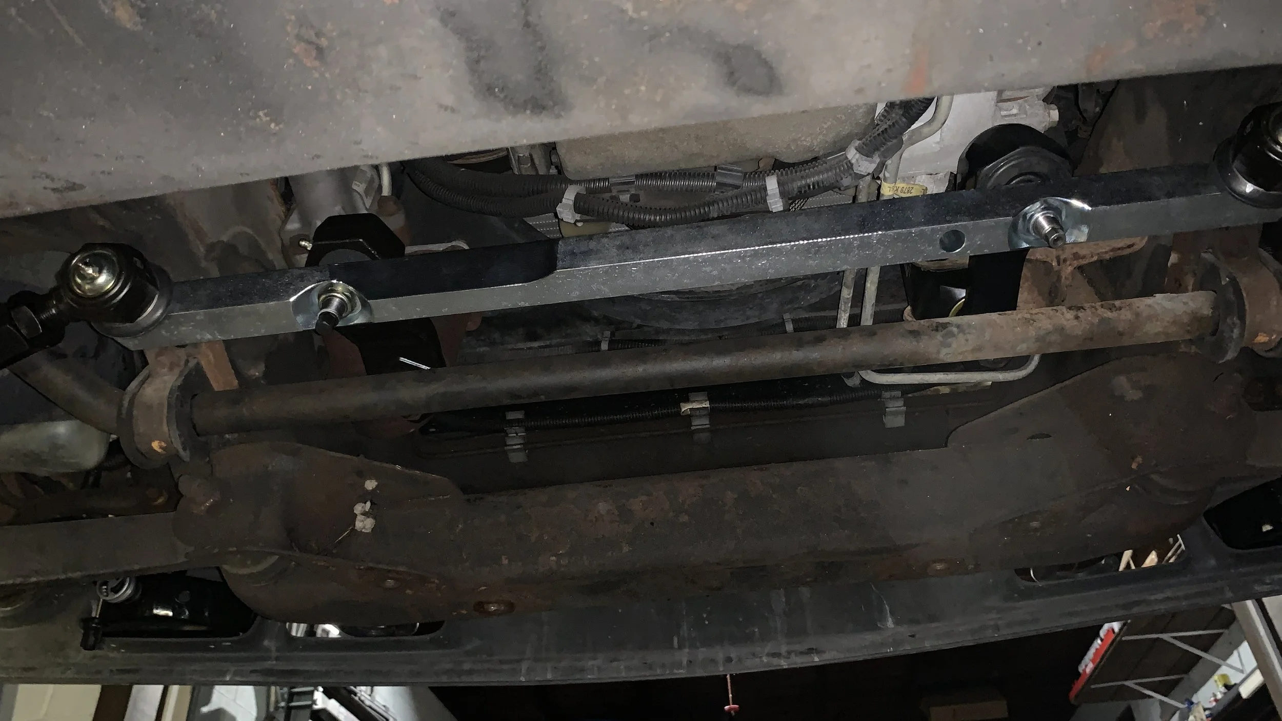 Underneath view of a vehicle's suspension system and components, including a metal sway bar and brackets.