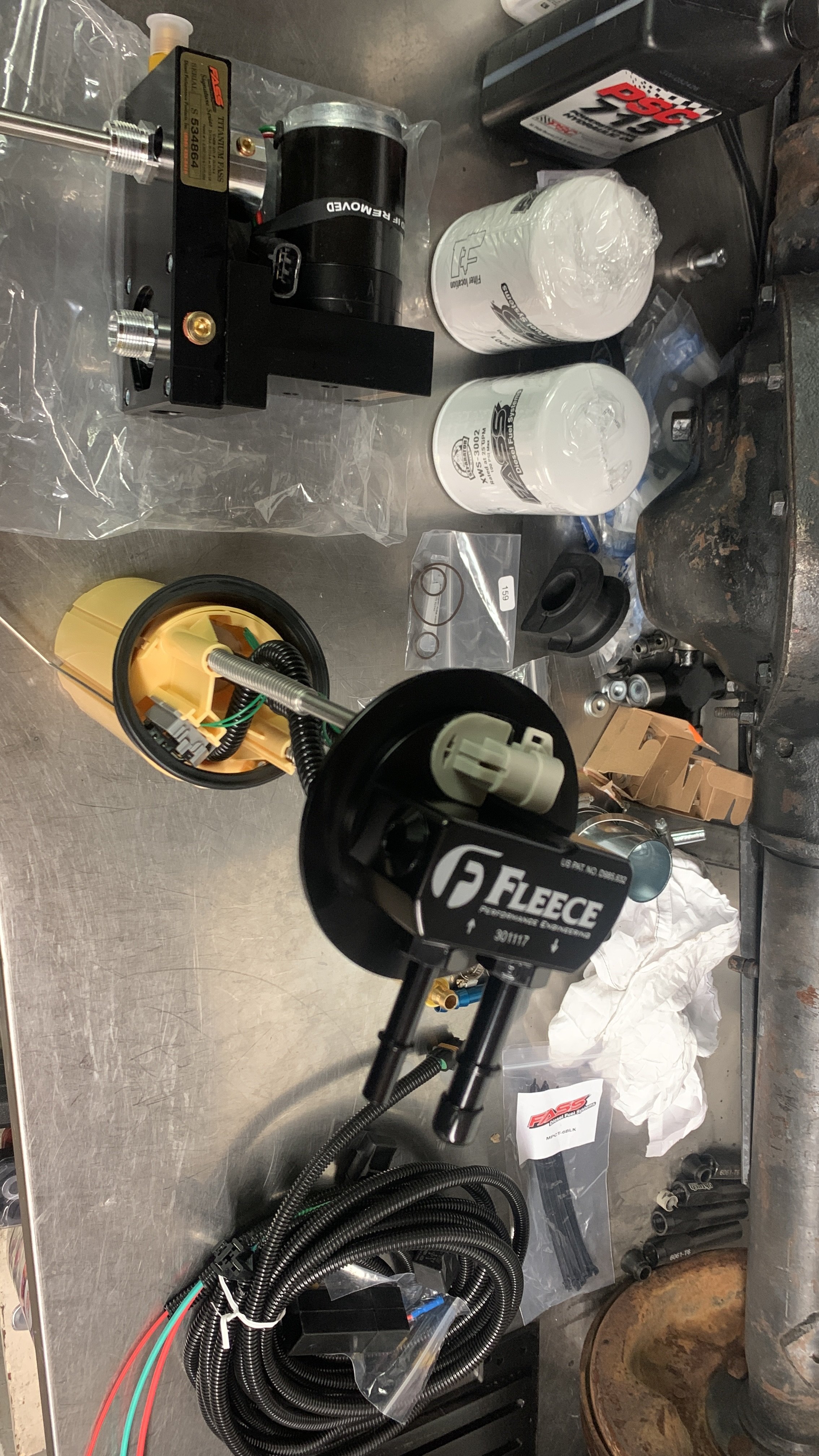 An automotive workbench with various mechanical and electrical parts, including fuel filters, wiring harnesses, a pump, and other engine components, along with tools and supplies.