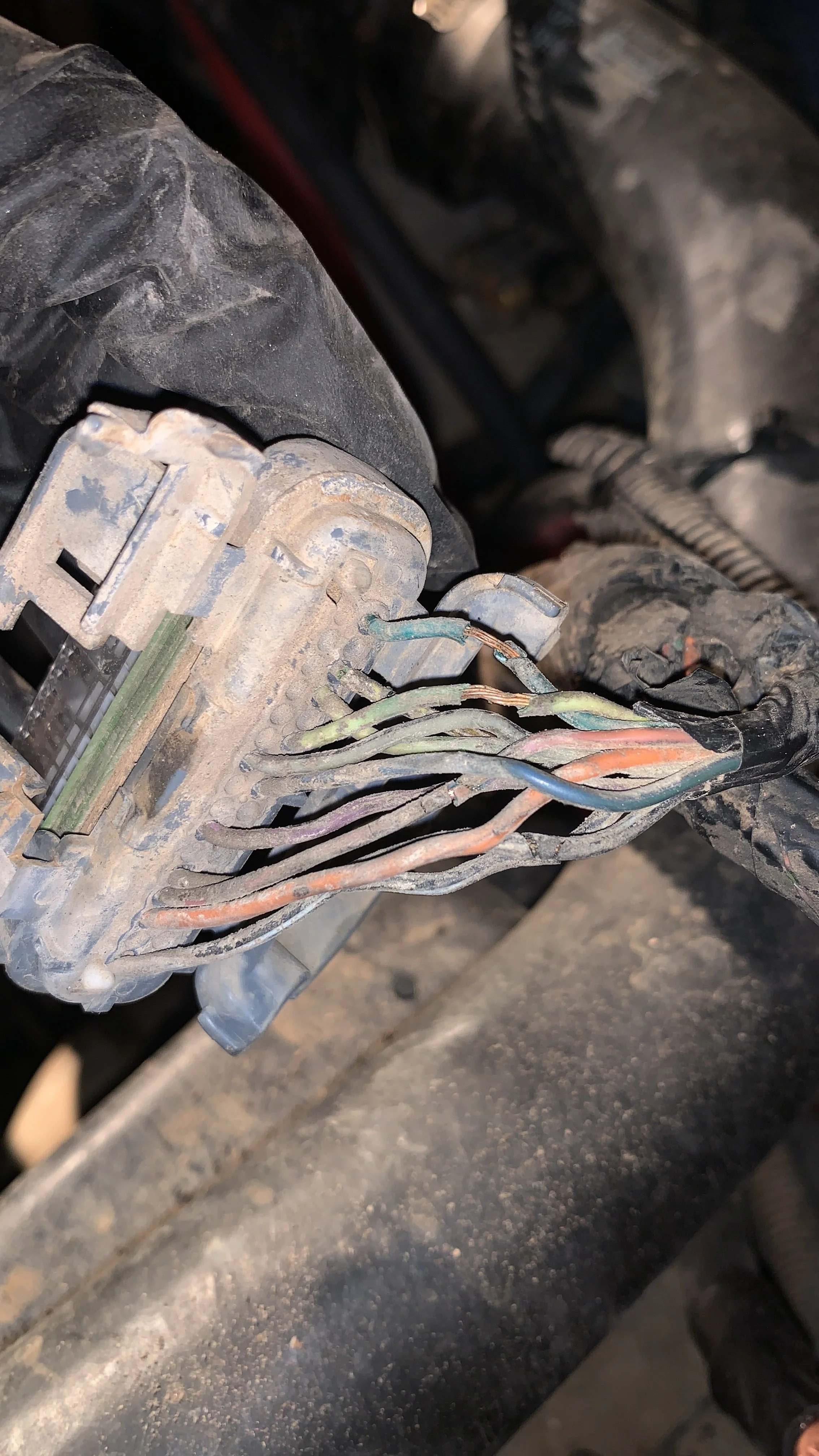 Deteriorated and disconnected electrical wires in a vehicle engine compartment.