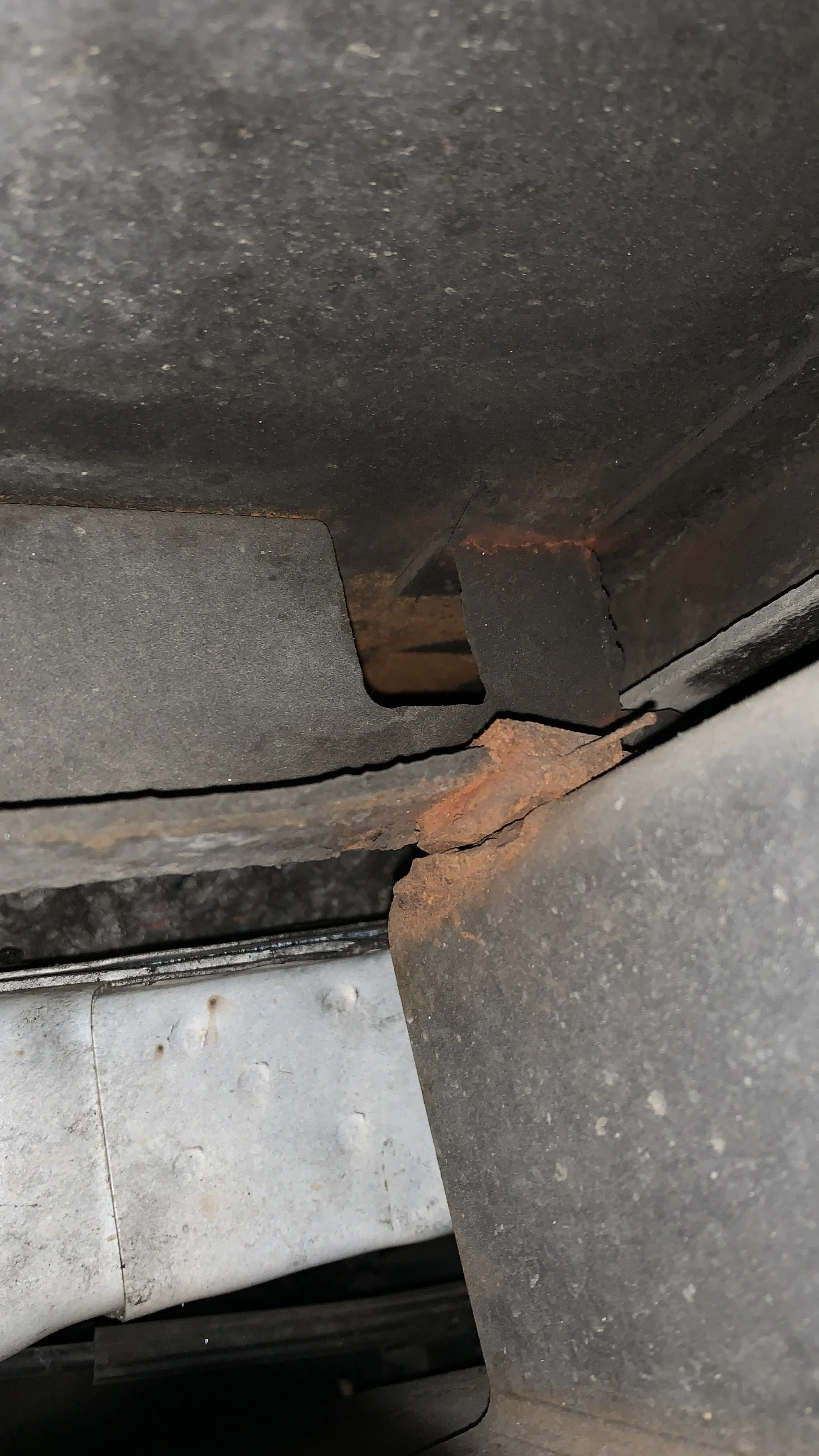 Close-up of rusted metal parts and possible frame damage underneath a vehicle.