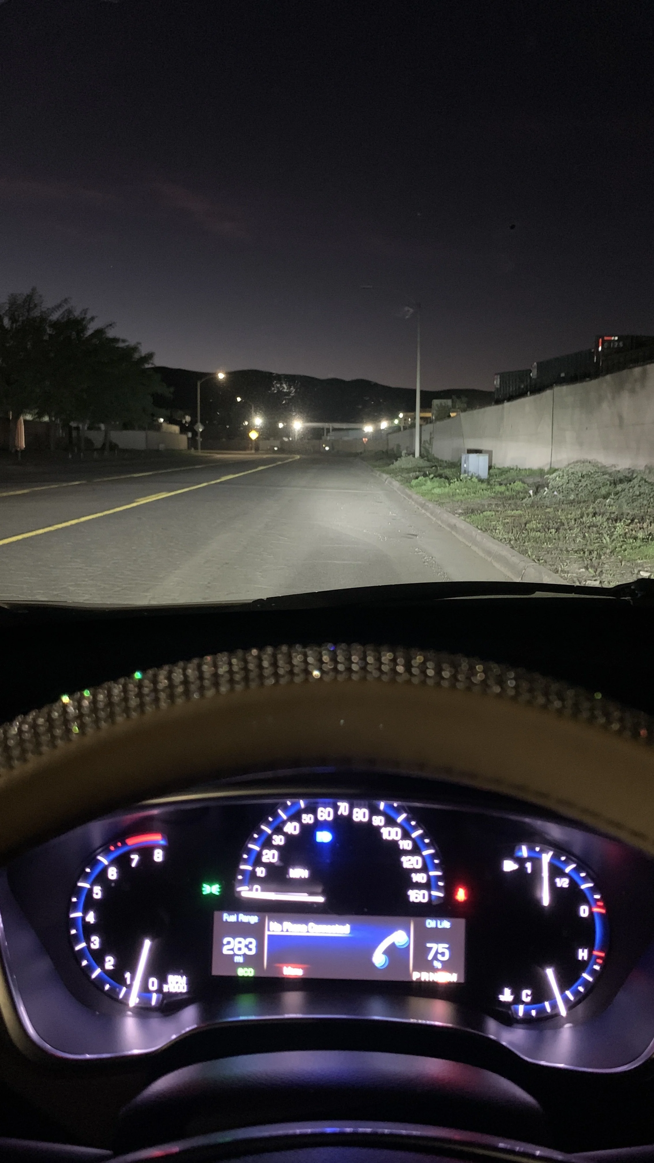 View from inside a car at night showing the dashboard illuminated, with the street ahead lit by streetlights and mountains in the distance.