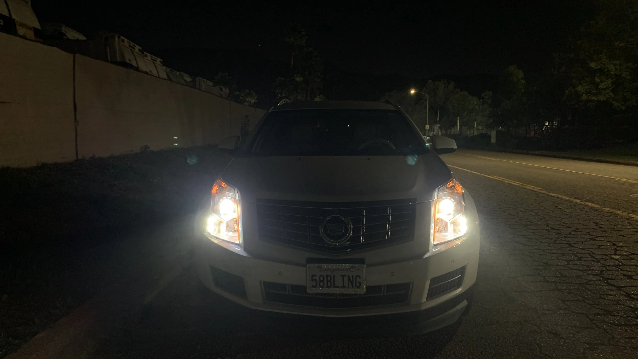 A white SUV with its headlights on parked on the side of a dark street at night.