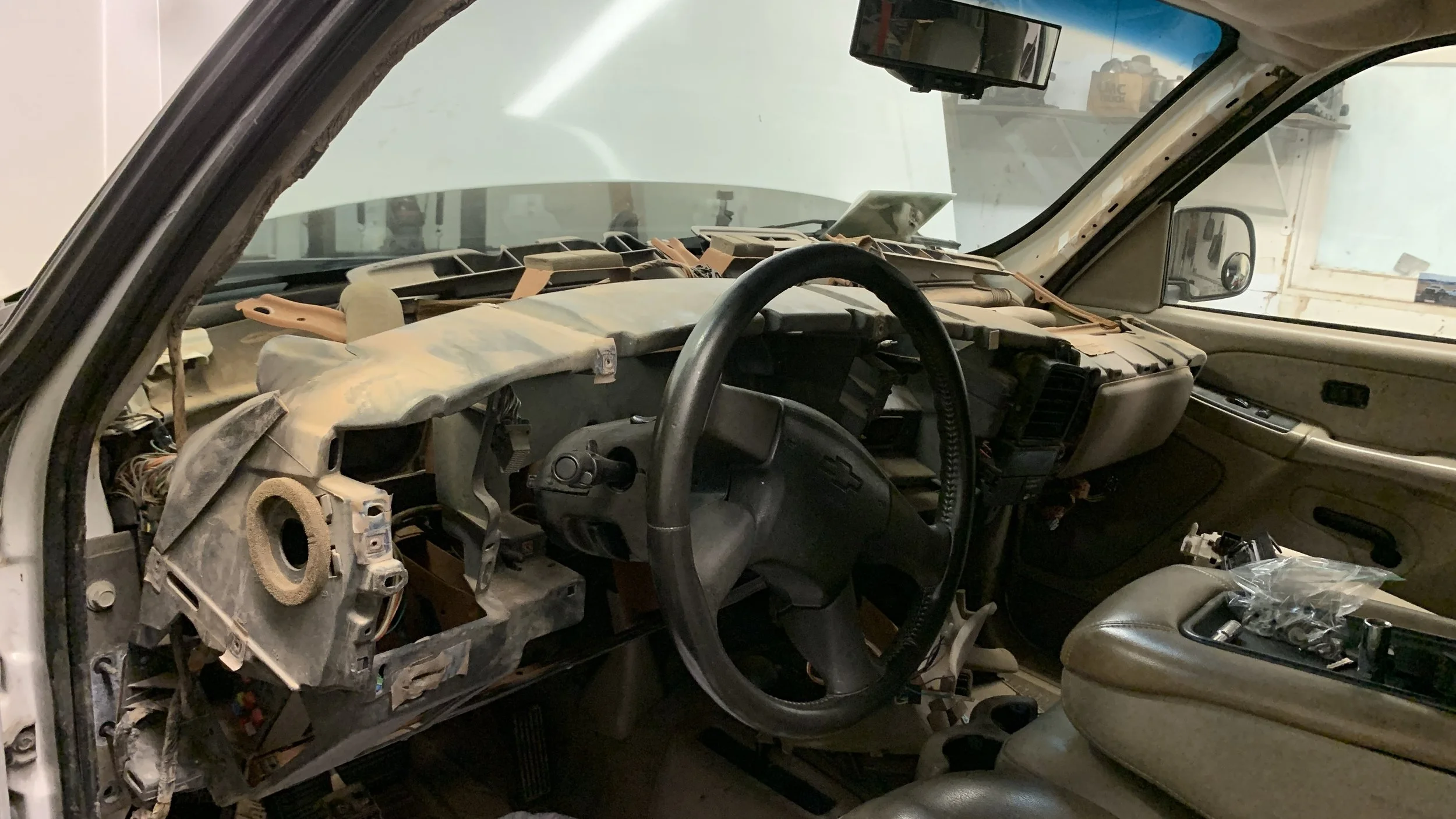 The interior of a Chevrolet vehicle in the process of being disassembled or repaired, with exposed dashboard components and a plastic bag on the center console.