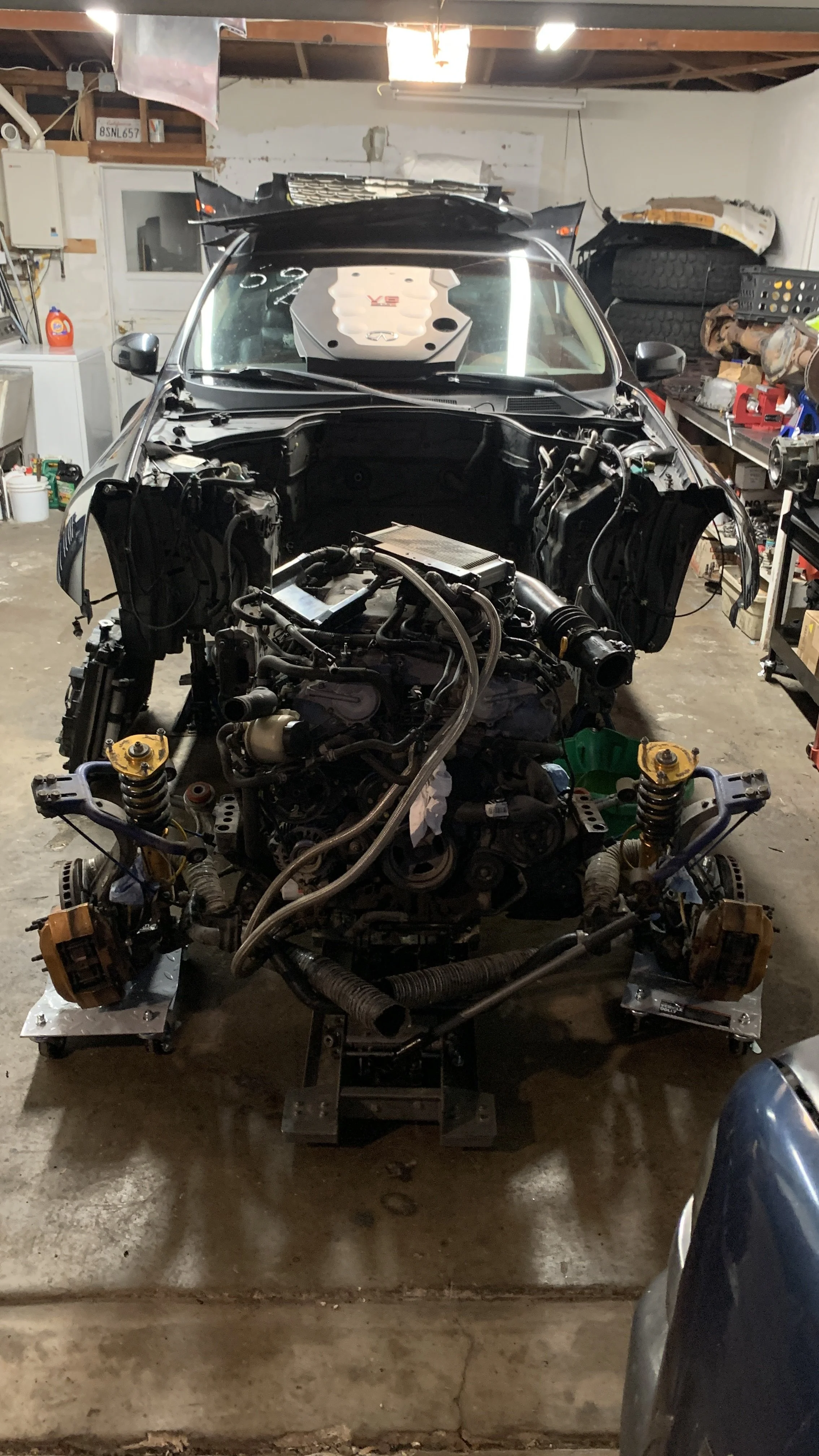 A car engine, partially disassembled, in a garage with tools and car parts around.