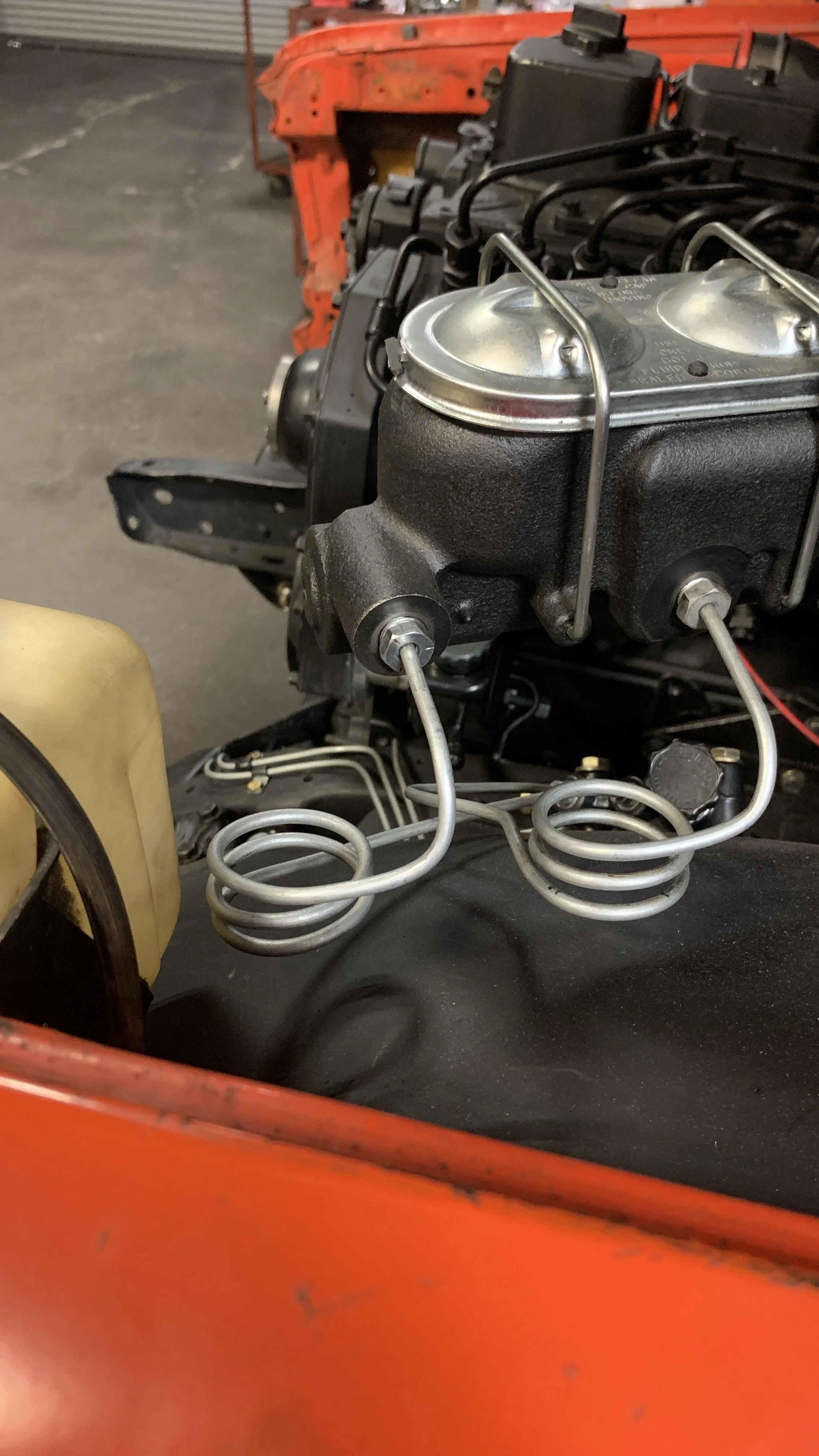 Close-up of a vintage car engine with parts, including black and metallic components, and orange bodywork visible in the background.