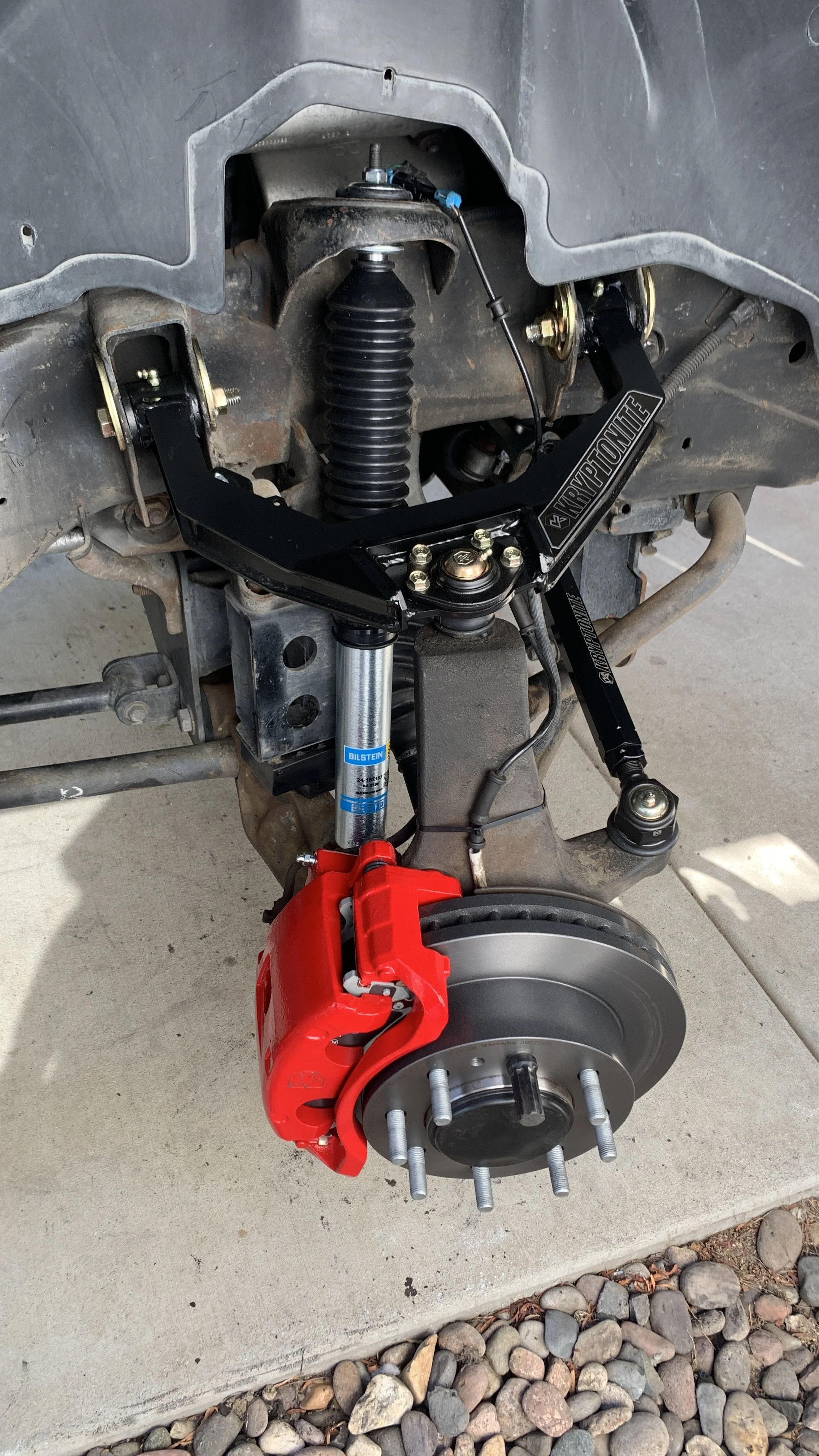 A car's front suspension system showing the brake caliper, brake rotor, and a custom black suspension control arm.