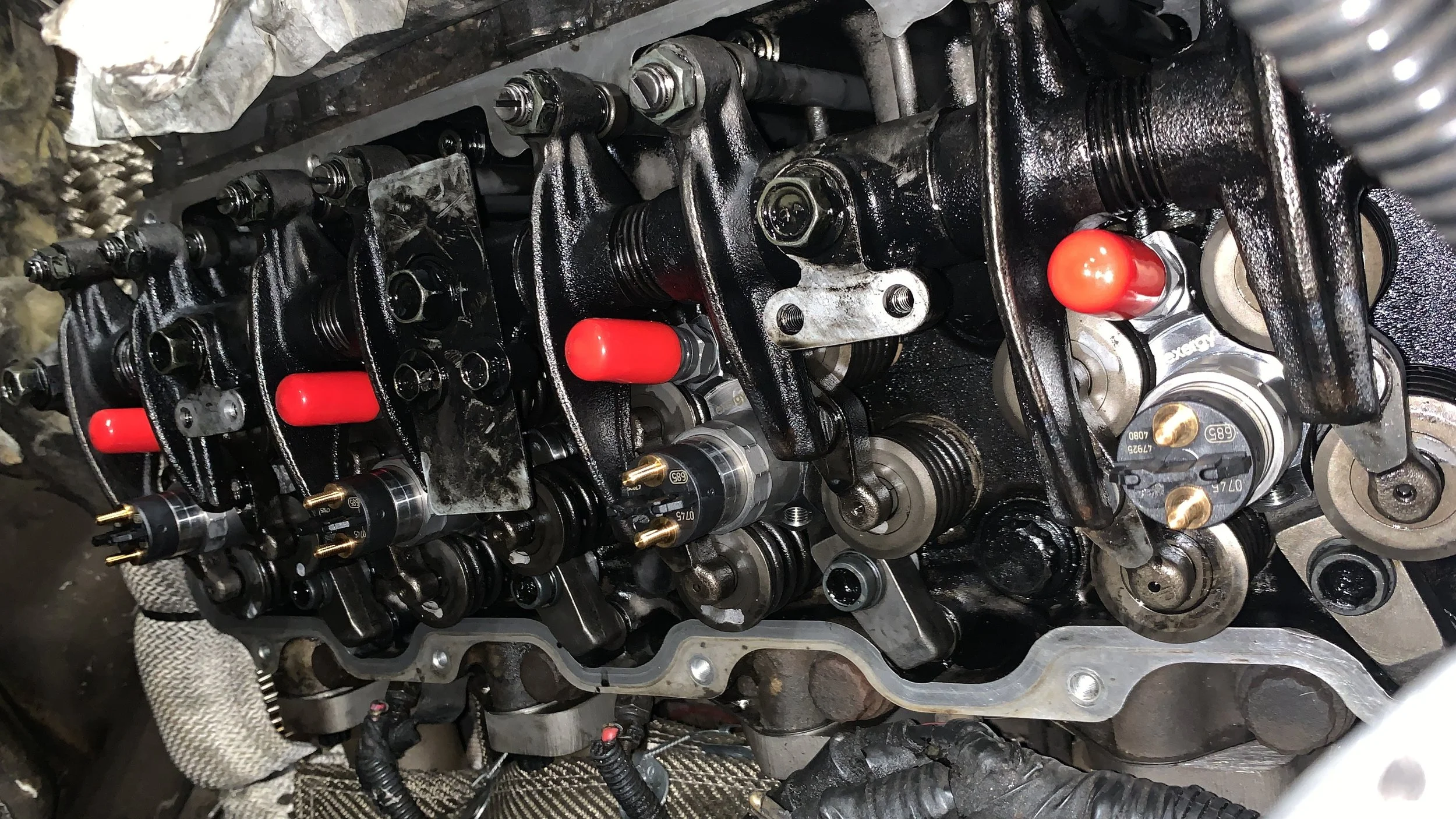 Close-up view of an engine's valvetrain components, including rocker arms, camshaft, and fuel injectors, with some parts covered in oil and grime.