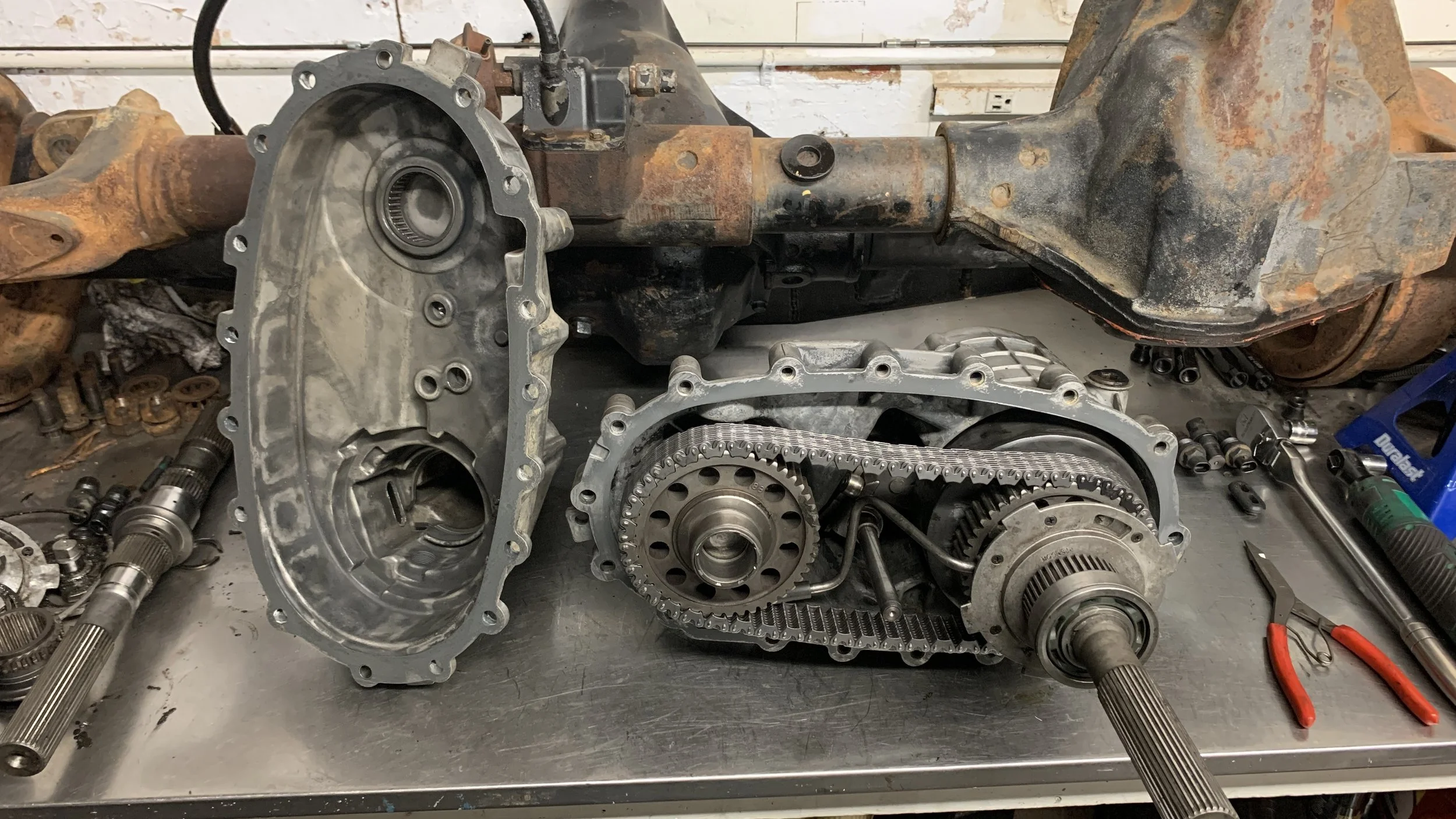 Disassembled automotive transmission parts on a workbench, with tools and mechanical components around.