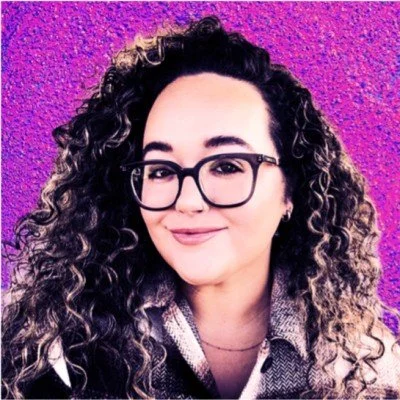 Ameliane smiles at the camera, she has glasses and dark curly hair.