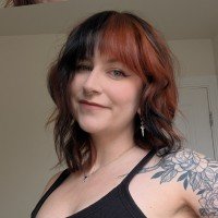 Stacey smiles at the camera. They have black and red hair.