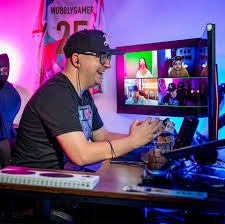 Wobbly sits at a desk lit with purple LEDs. He wears a cap and is laughing and gaming.