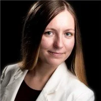 Bianca smiles at the camera. She has long brown hair and wears a white jacket.