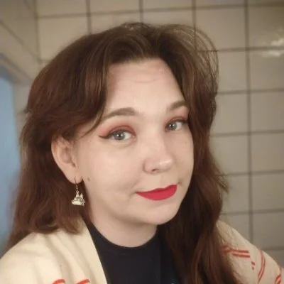 Harriet smiles at the camera, she wears red lipstick and has long brown hair.
