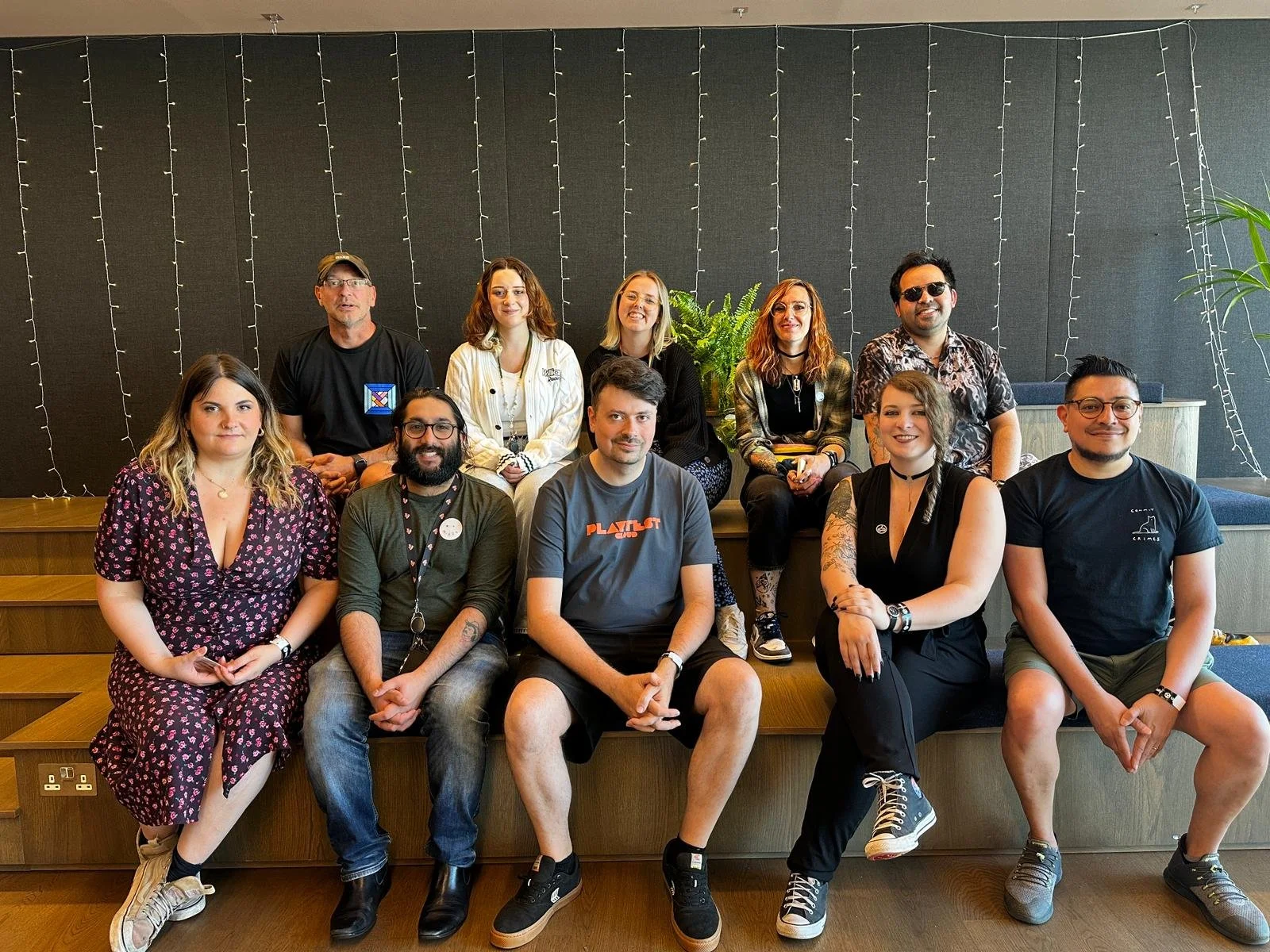 The Gathering organisers and volunteers for 2025, sitting on bleacher seating in front of string lights, smiling.