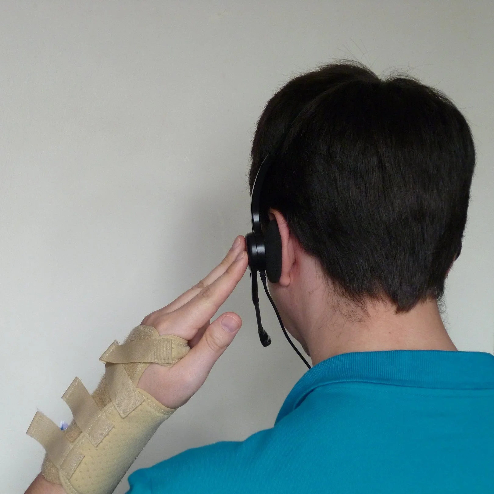 Victor faces away from the camera, wearing a headset and holding it with a hand wearing a brace.