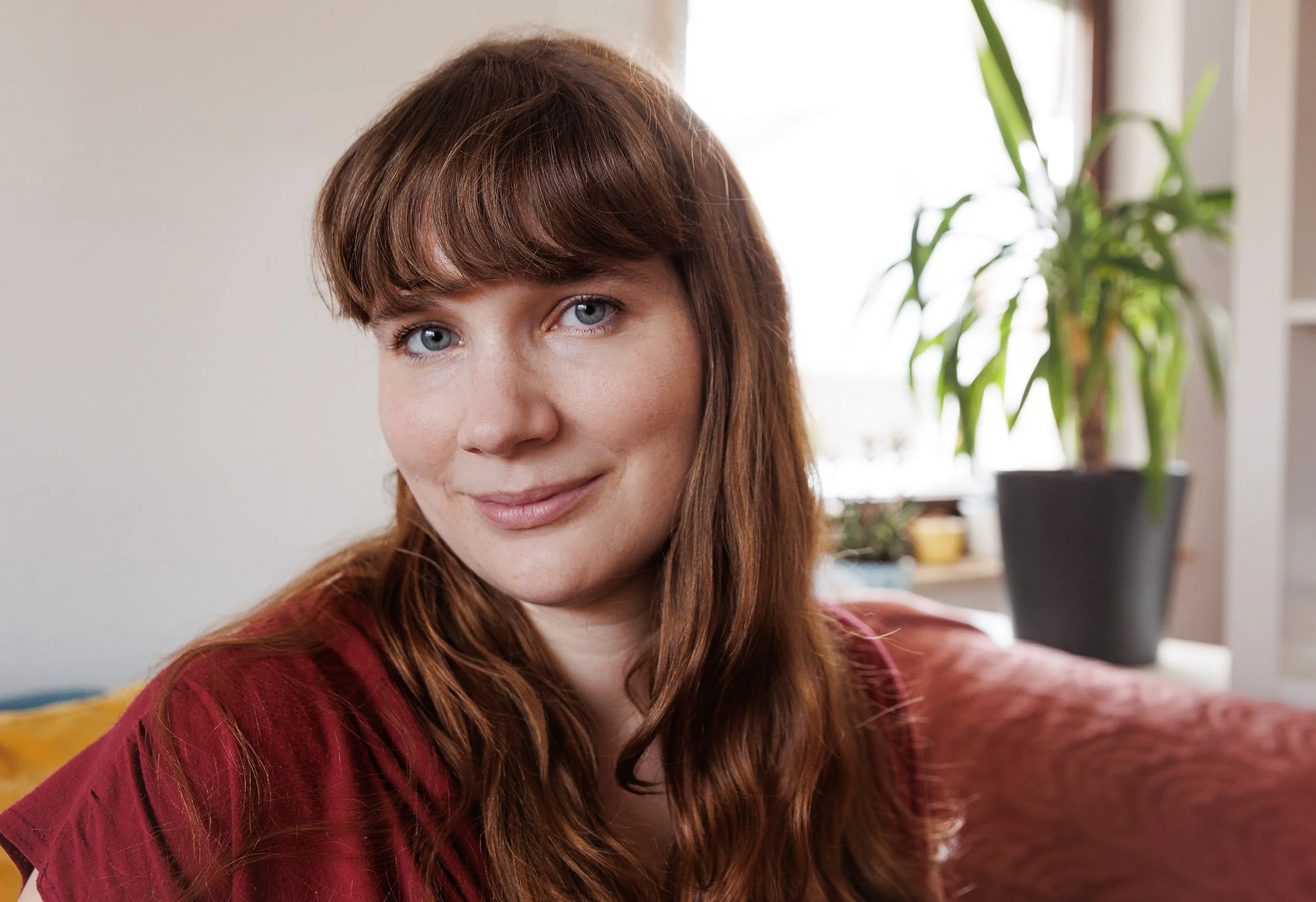 Anni smiles at the camera. She has long brown hair and wears a red top.