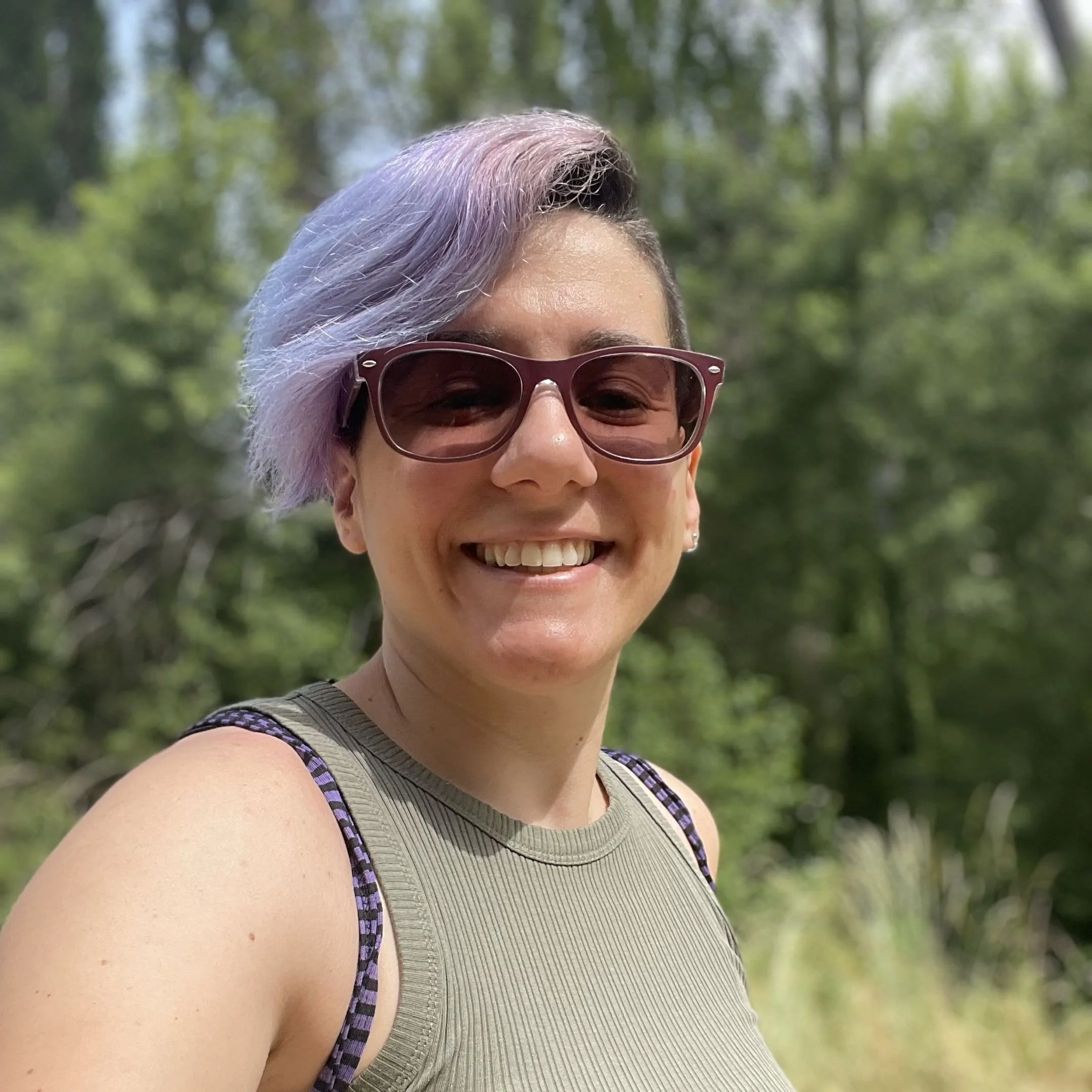 Jennifer smiles at the camera. She has short, lilac hair and wears sunglasses.