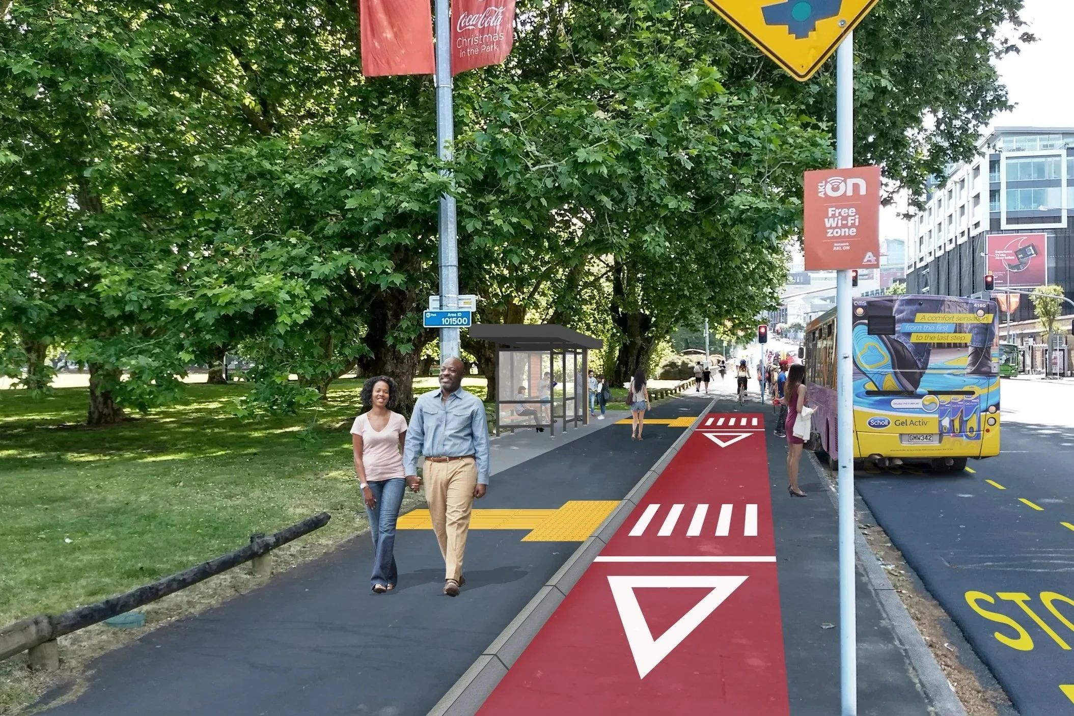 A city sidewalk with a red bike lane marked with white symbols and text, a bus parked on the right, pedestrians walking, and lush green trees in the background.