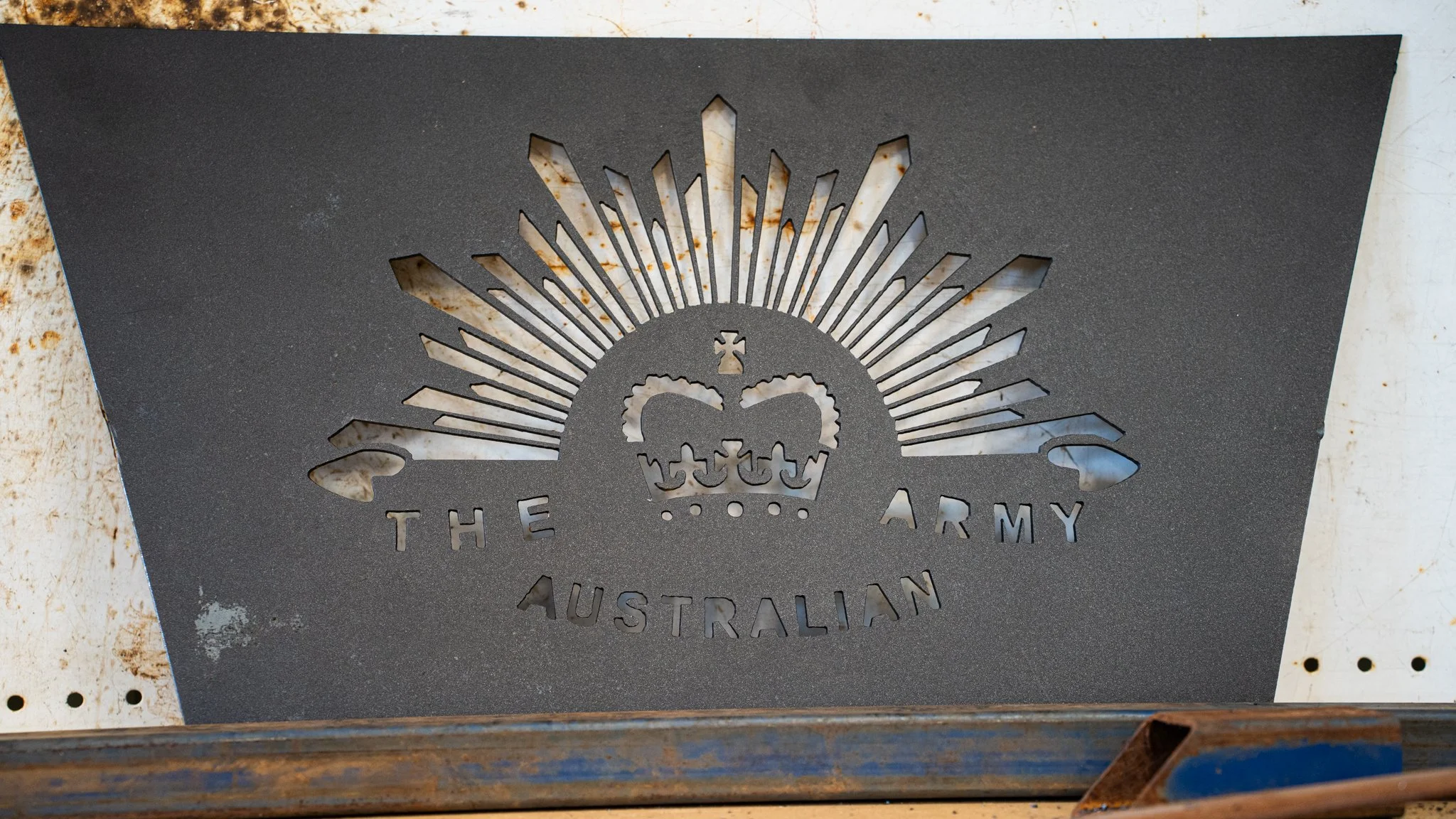 Black metal sheet with a cut-out design of a skull wearing a crown, surrounded by rays of light, with the words "The Army Australian" underneath.