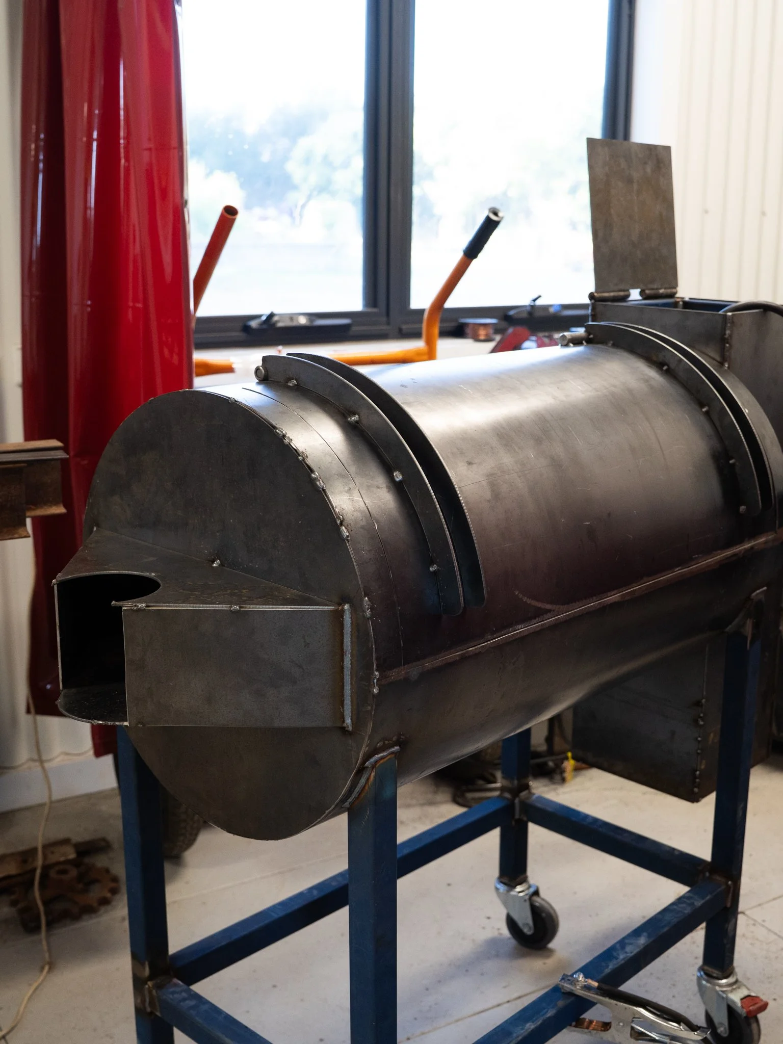 Large metallic machine or vessel on a blue wheeled platform with a window and building interior in the background.