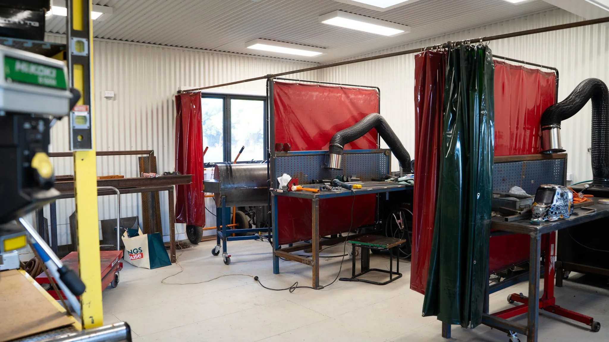 A workshop with workstations separated by red and green welding curtains, tools, equipment, and workbenches.