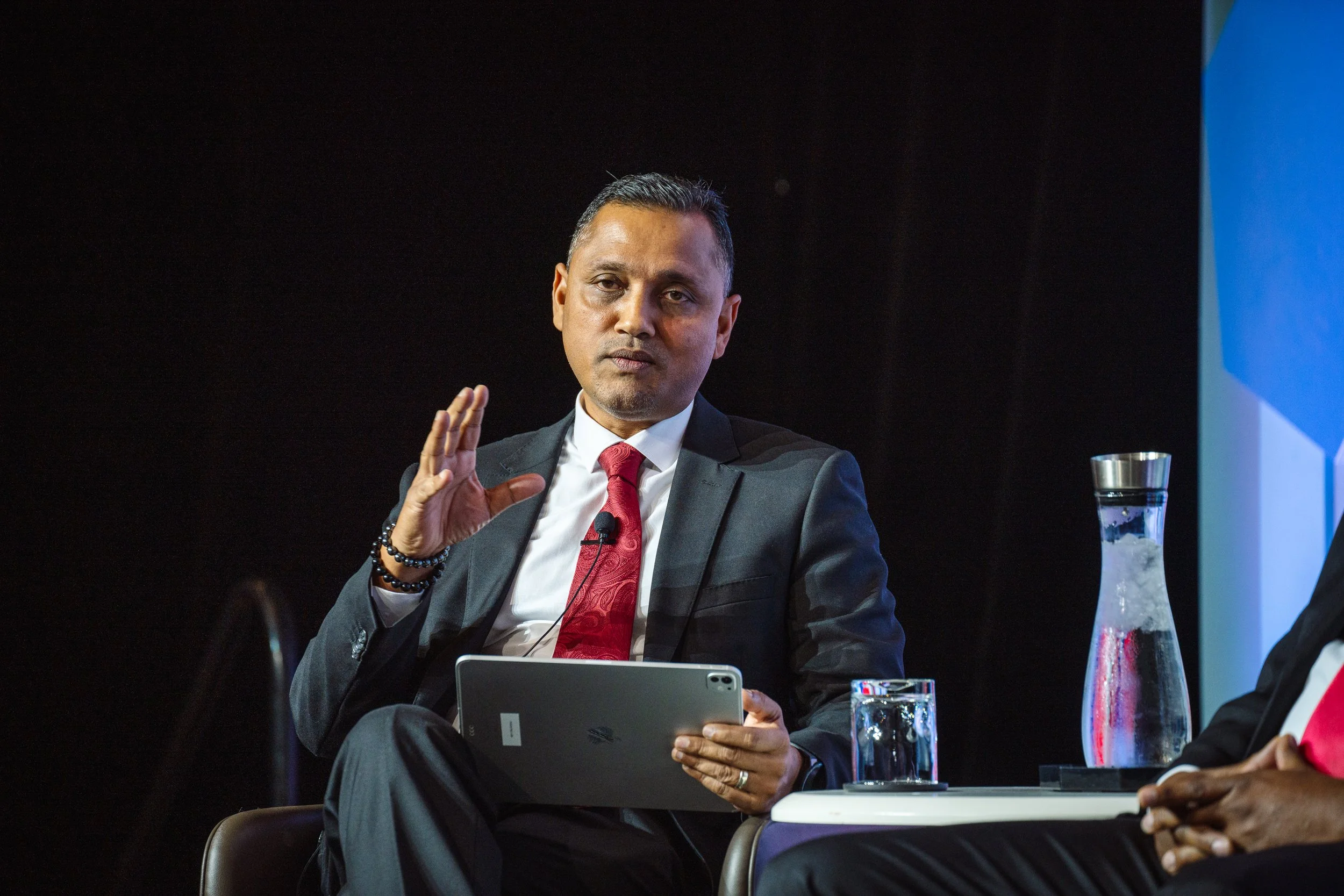 Dr. Inshan Meahjohn speaking at an international digital government conference, presenting on stage with a tablet