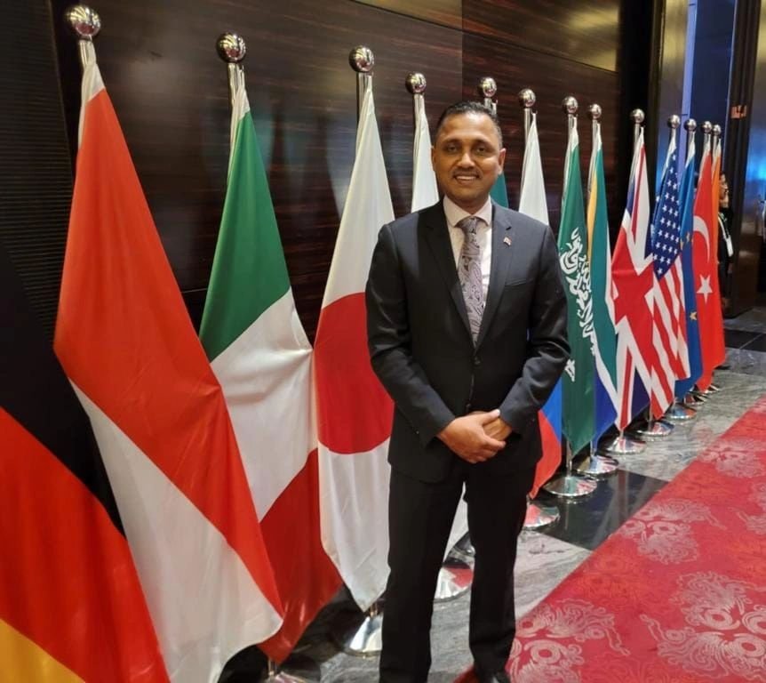 Dr. Inshan Meahjohn at the White House Global Digital Government Forum in Washington D.C., standing with international flags