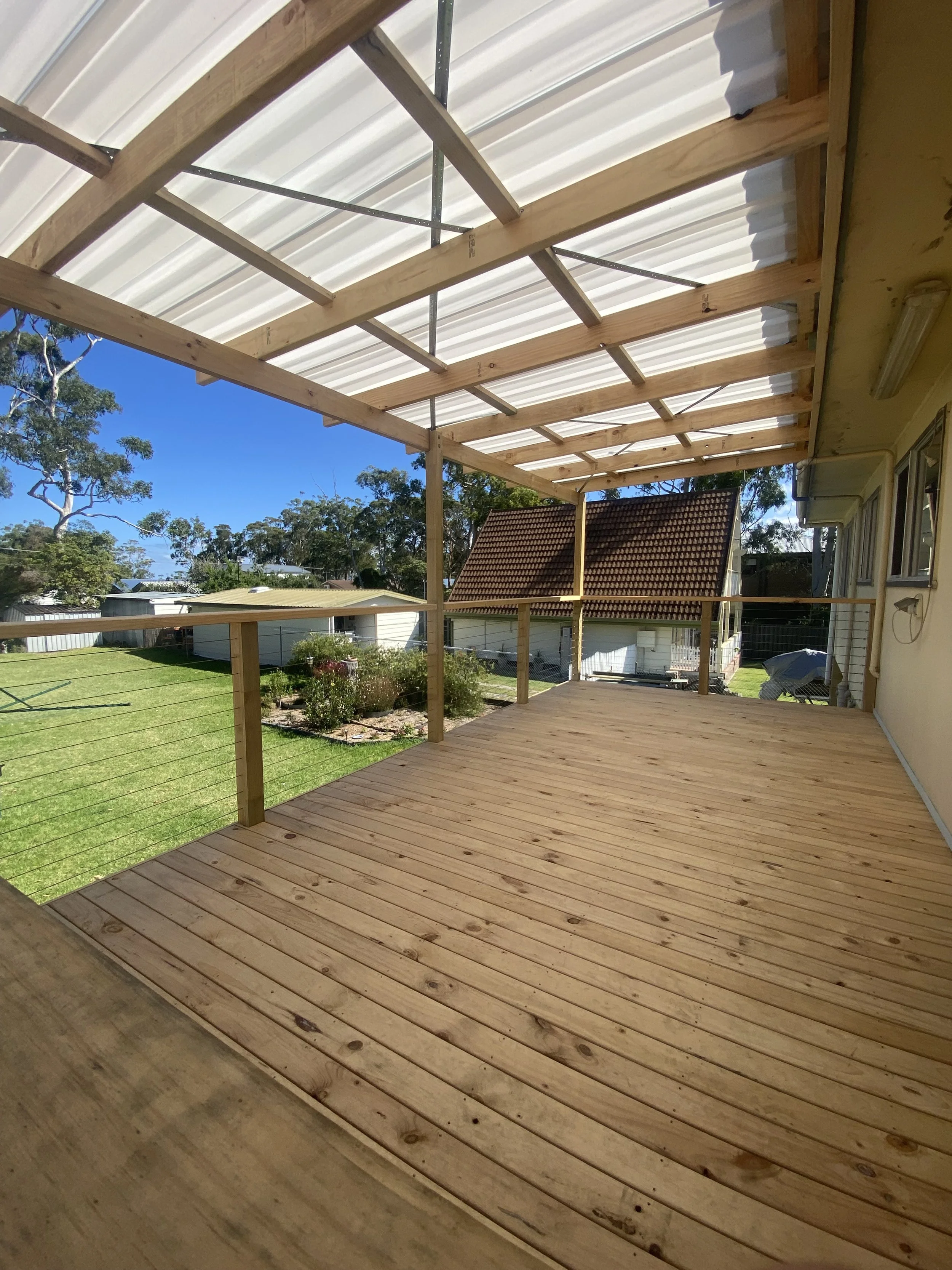Wooden deck with exposed rafters under a partially completed roof structure, overlooking a backyard with trees, a shed, and neighboring houses.