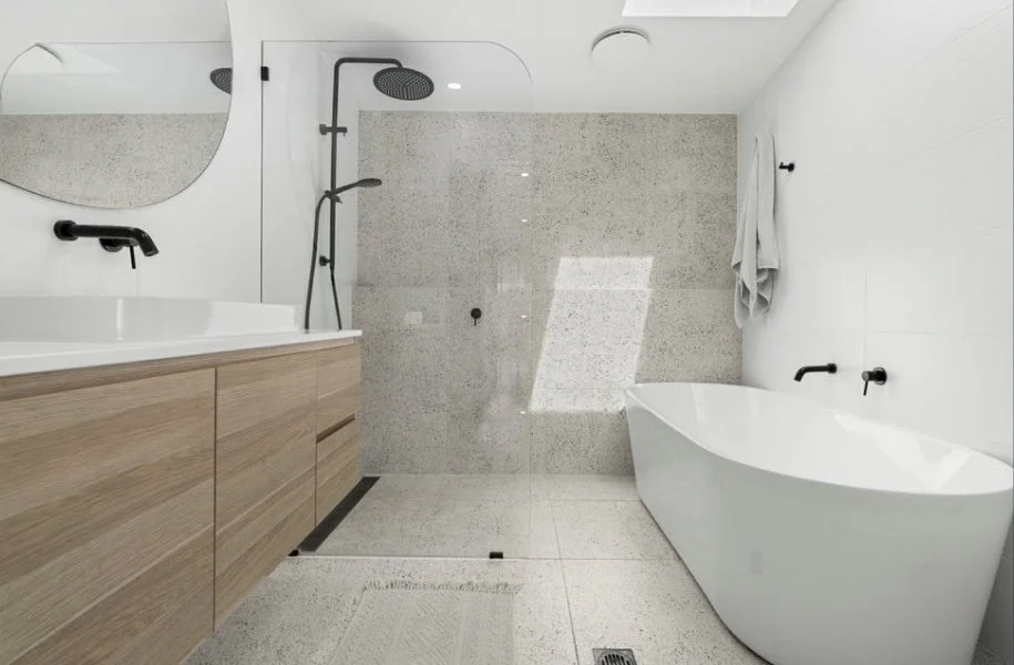 Modern bathroom with wood vanity, black fixtures, walk-in shower with glass door, and free-standing bathtub.