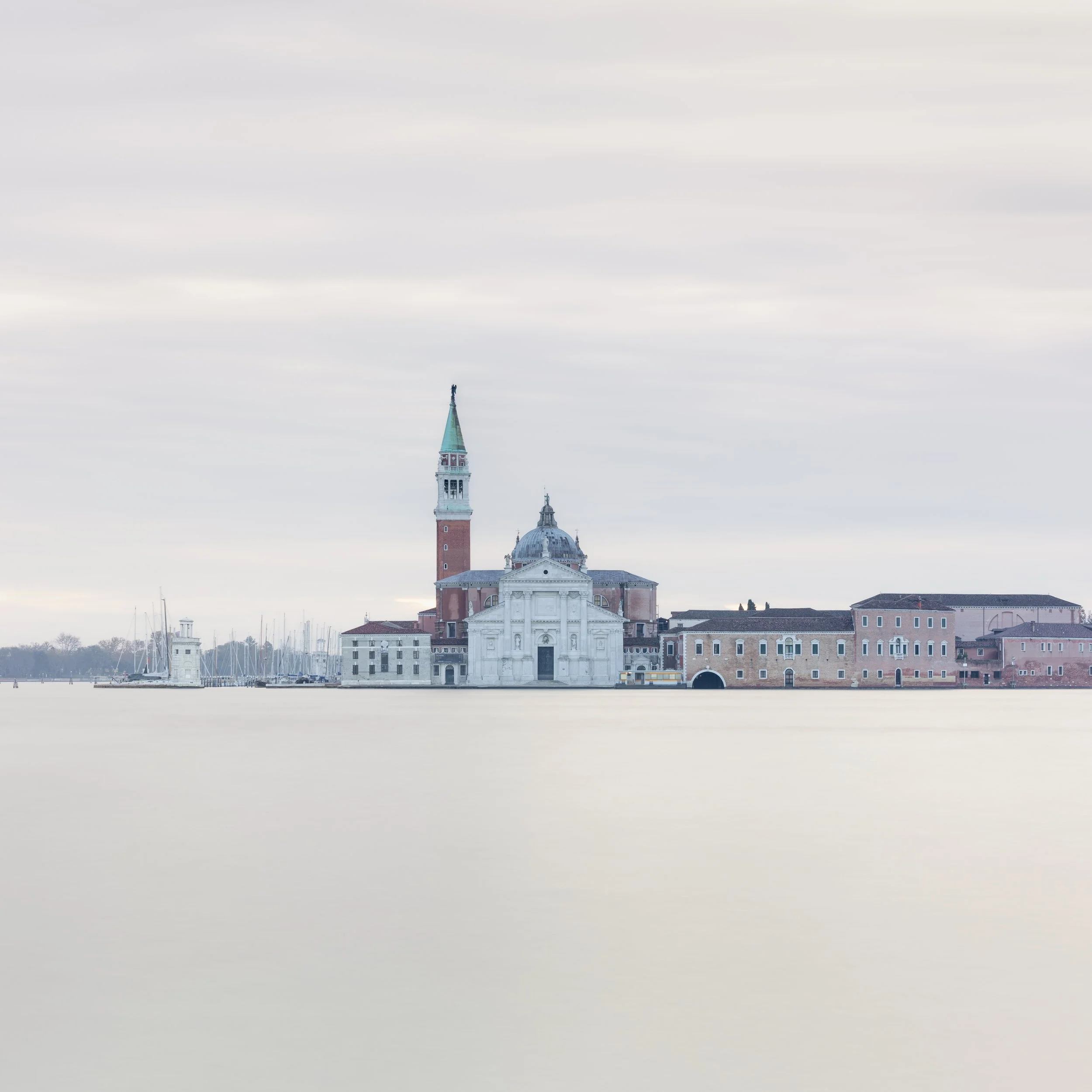 View of the island of San Giorgio Maggiore in Venice, Italy, with church and bell tower, over water with sailboats and cloudy sky