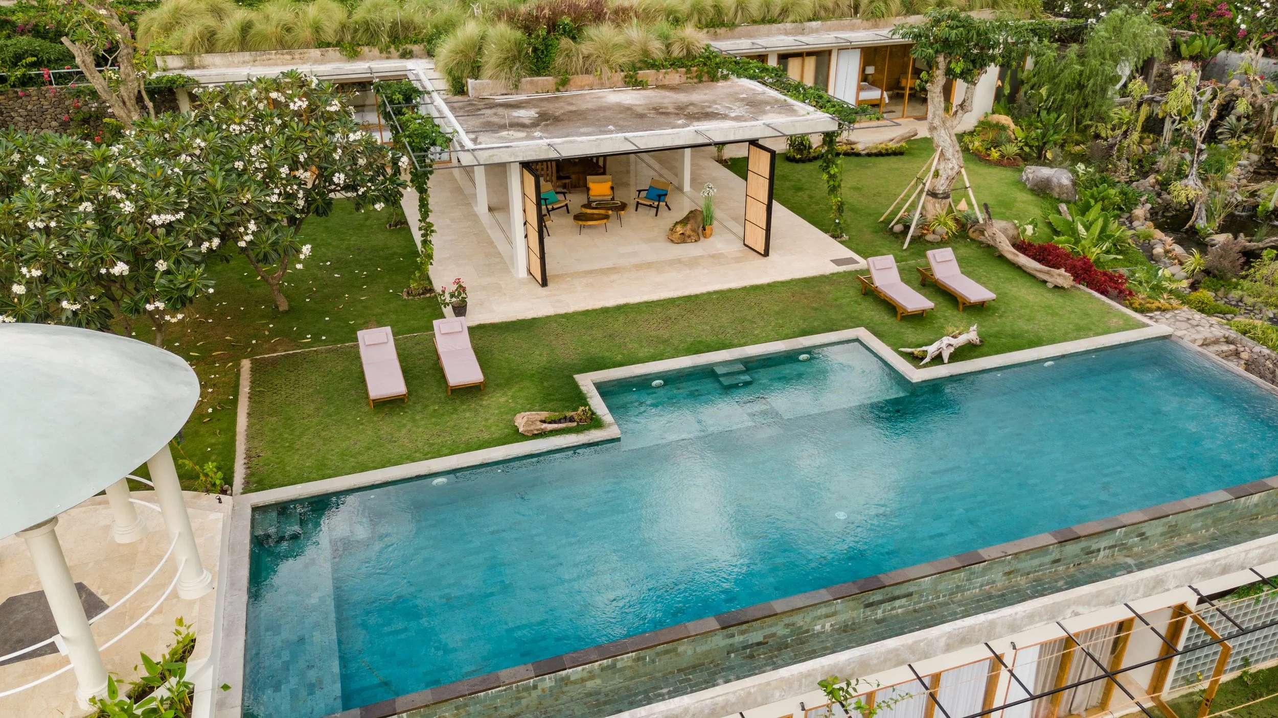Aerial view of a luxurious backyard with a swimming pool, outdoor lounge area, landscaped garden, and a small fountain with a horse sculpture.