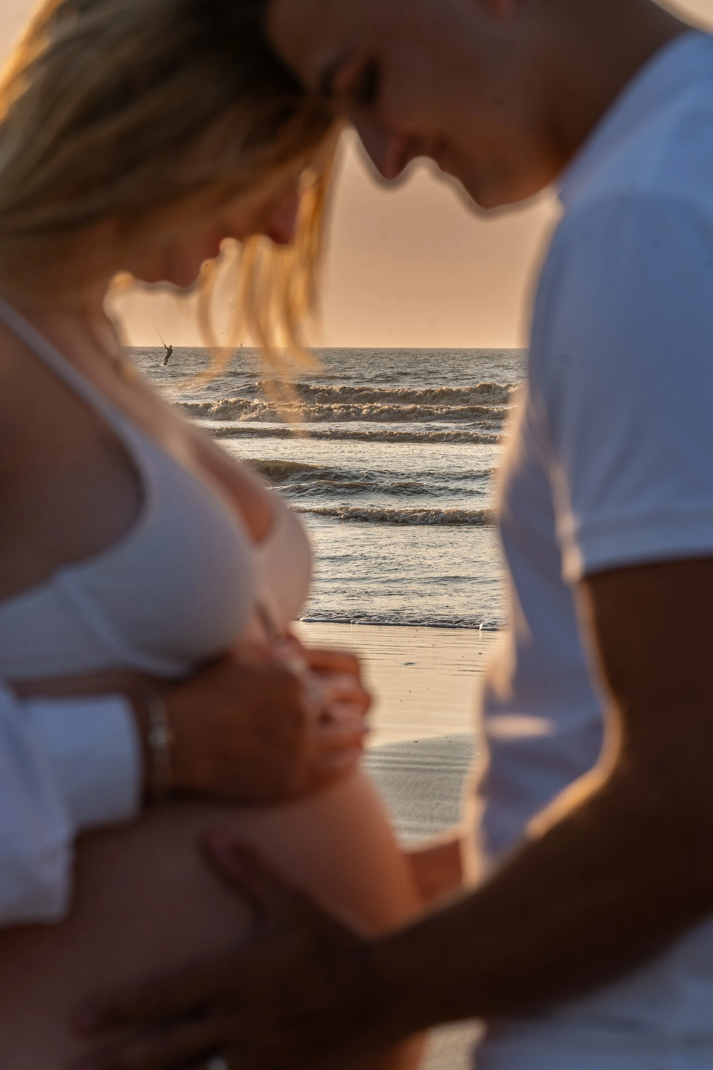Un couple regardant une échographie, sur une plage au coucher du soleil.