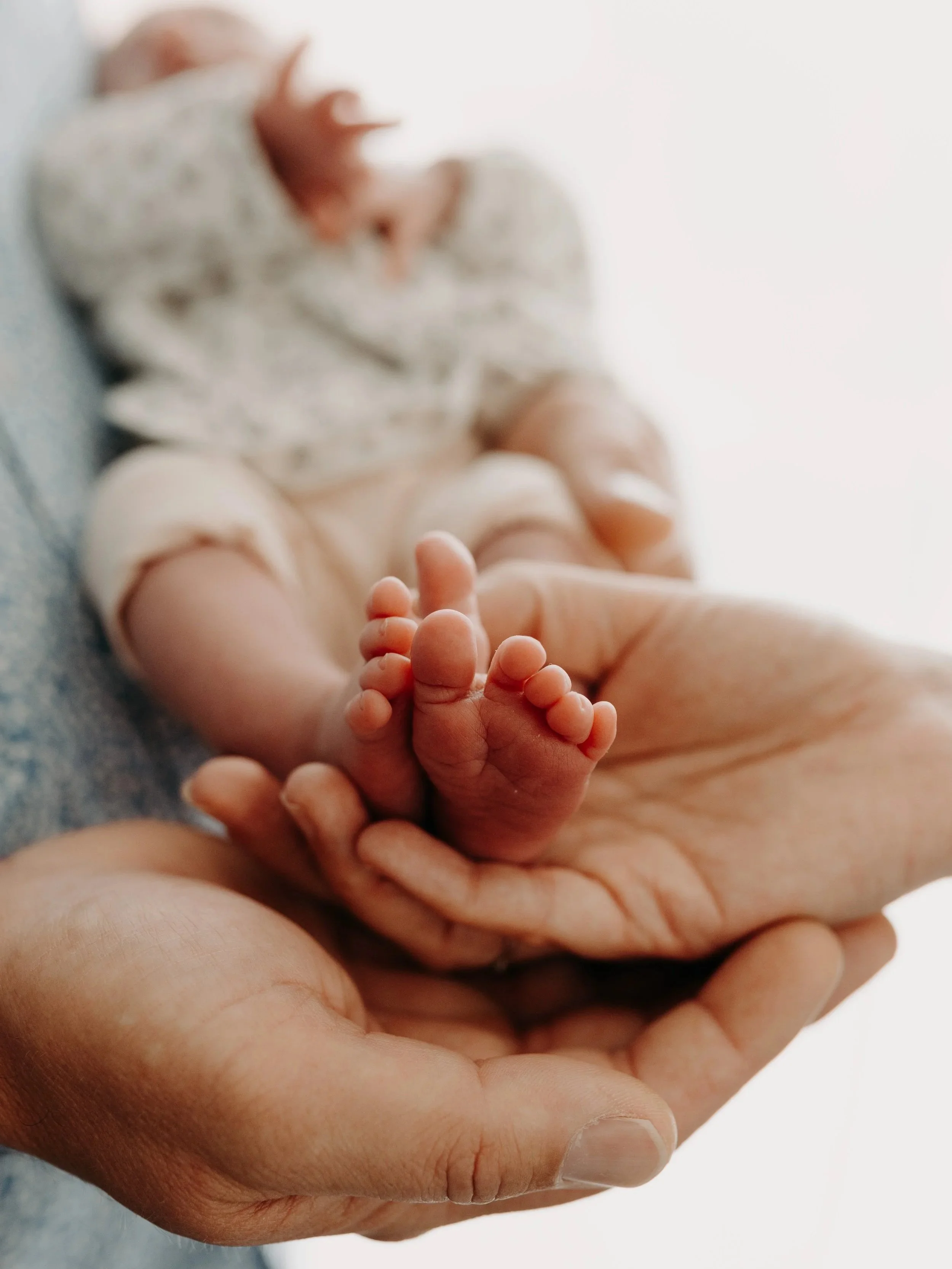 Une main adulte tient doucement une toute petite main de bébé, symbole de tendresse et de protection.