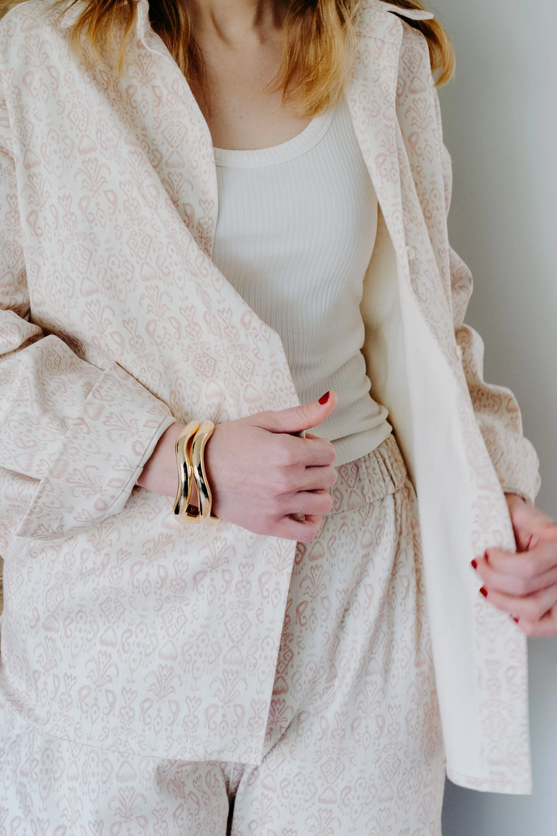 Une femme portant un pantalon et un blazer à motifs délicats et un t-shirt blanc, avec des bracelets dorés à la main gauche.