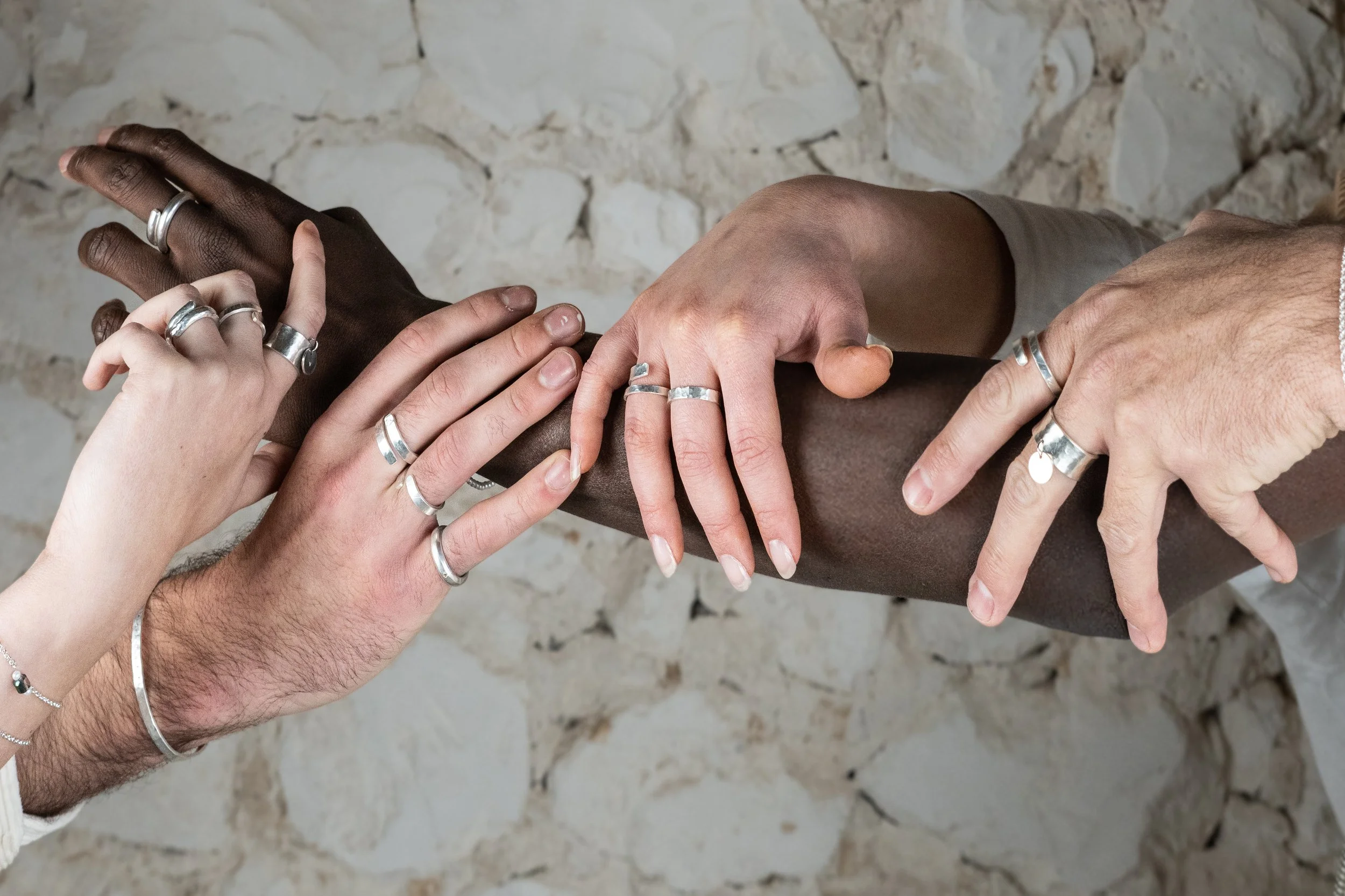 Main d'hommes et femmes de différentes origines portant des alliances en argent, se joint dans une démonstration d'unité, avec un fond en pierre beige.