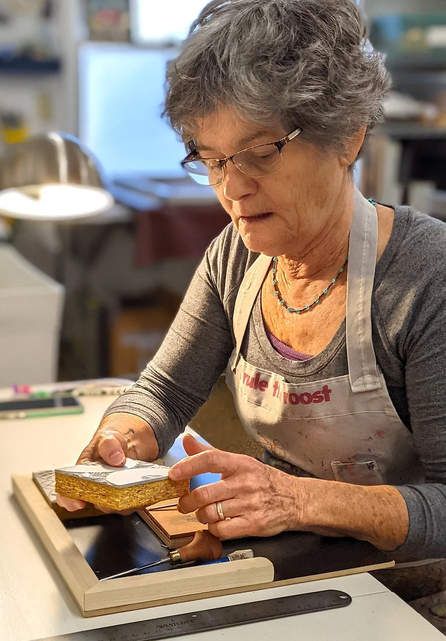 Printmaking artist Jeanne Brady carving a linoleum block at a studio table, preparing fabric printing designs