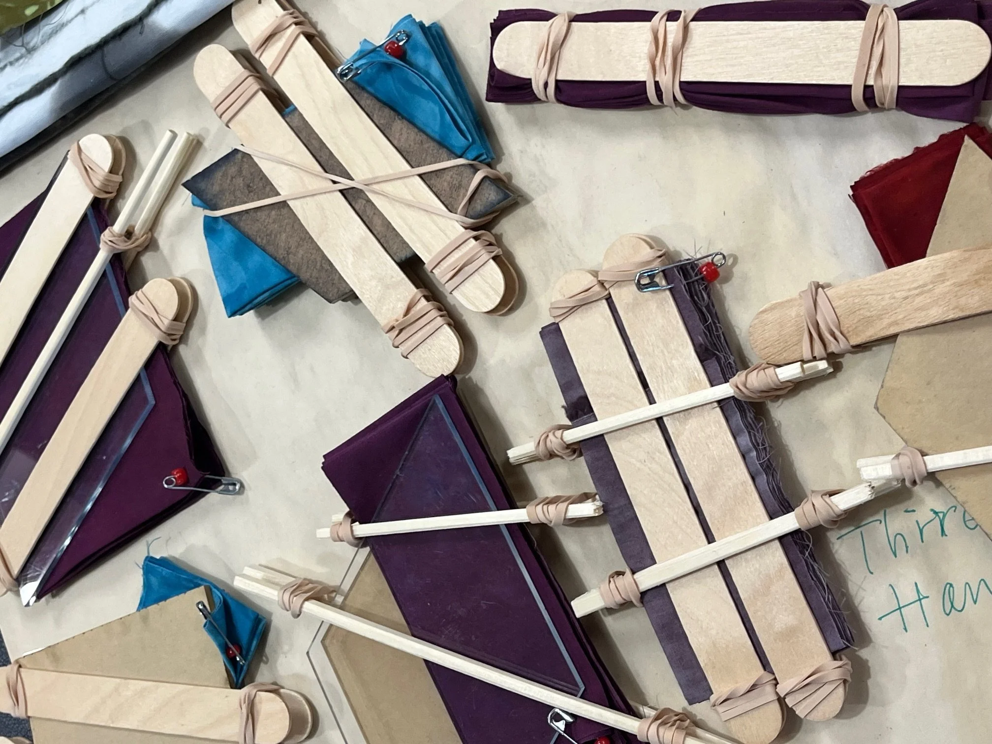Fabrics folded and resisted for shibori,  laid out on a table, secured with rubber bands and tongue depressors