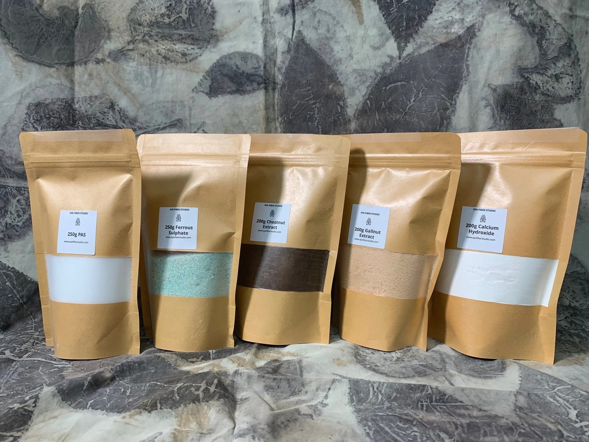 Natural dye mordants in labeled kraft pouches including ferrous sulphate, gallnut extract, chestnut extract, calcium hydroxide, and PAS for textile dyeing.