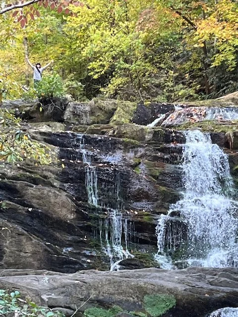 Mountain waterfall cascading over moss-covered rocks surrounded by autumn forest, representing the Blue in the Mountains fiber retreat in North Carolina