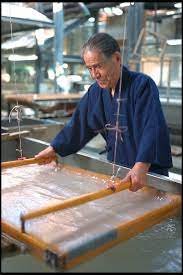 A man dressed in traditional Japanese clothing washing a large cloth or textile in a water basin.
