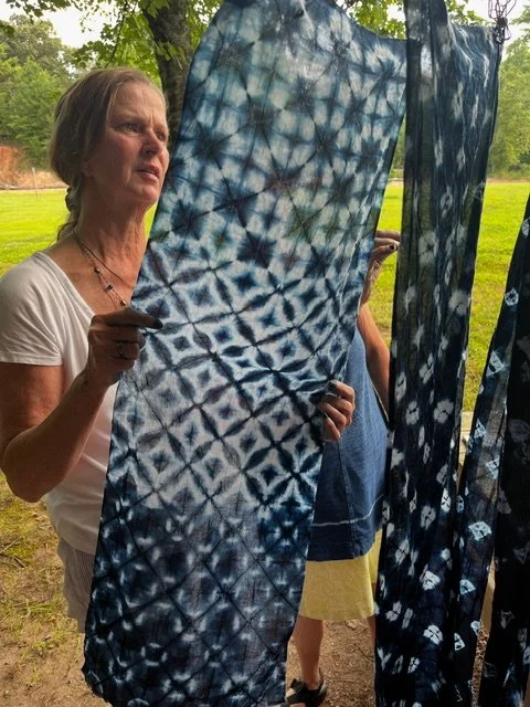 Woman holding up a large piece of indigo-dyed fabric with blue and white tie-dye pattern outdoors.