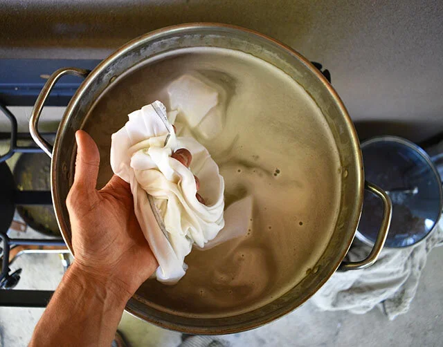 Person holding cloth over a metal pot getting ready to scour fabric, on a stovetop.