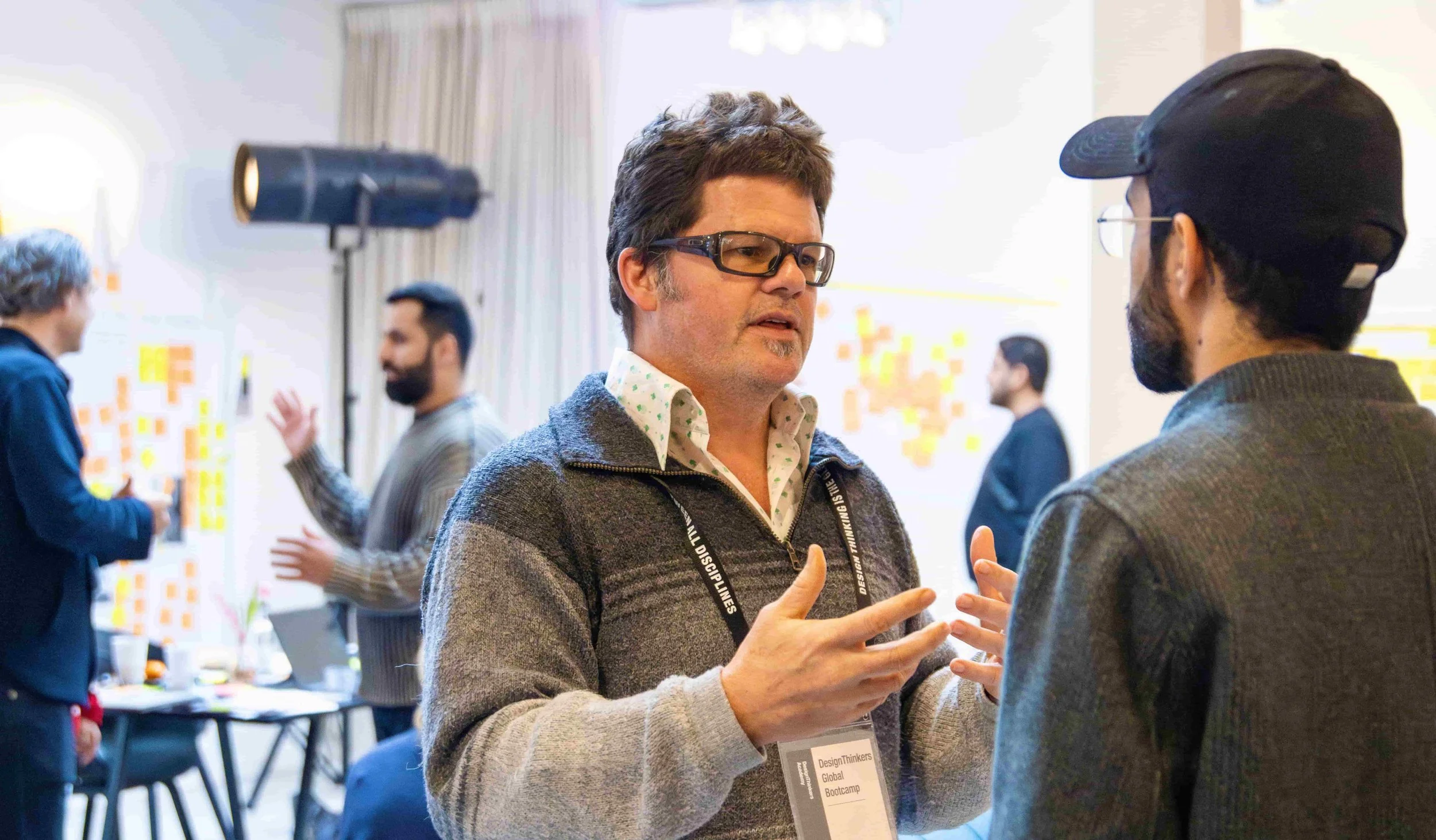 Two men engaged in conversation at a professional networking event, with others talking in the background.